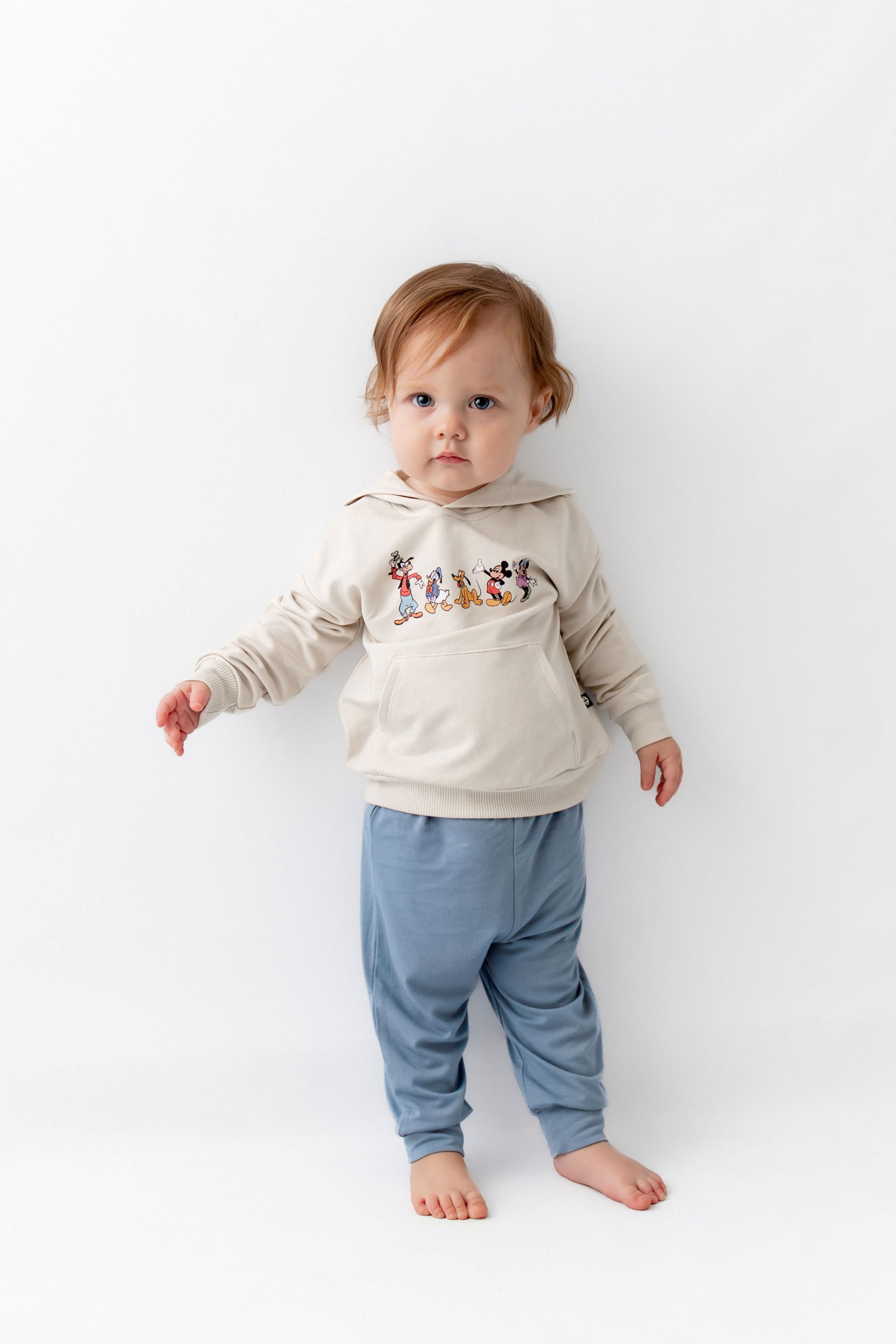 Toddler standing wearing mickey mouse friends hoodie with blue pants.