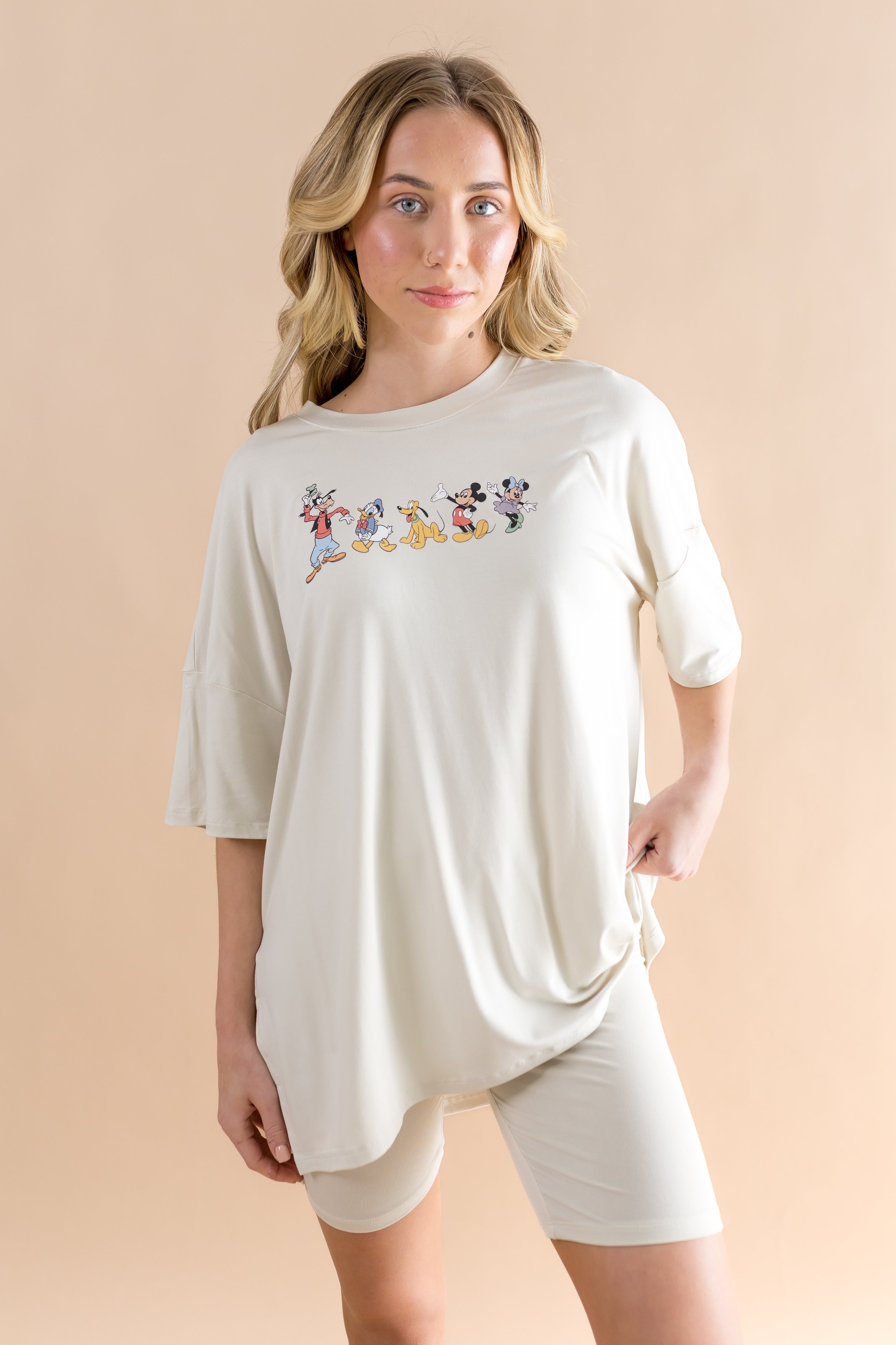 Woman wearing a white oversized t-shirt with cartoon character design and biker shorts on a beige background