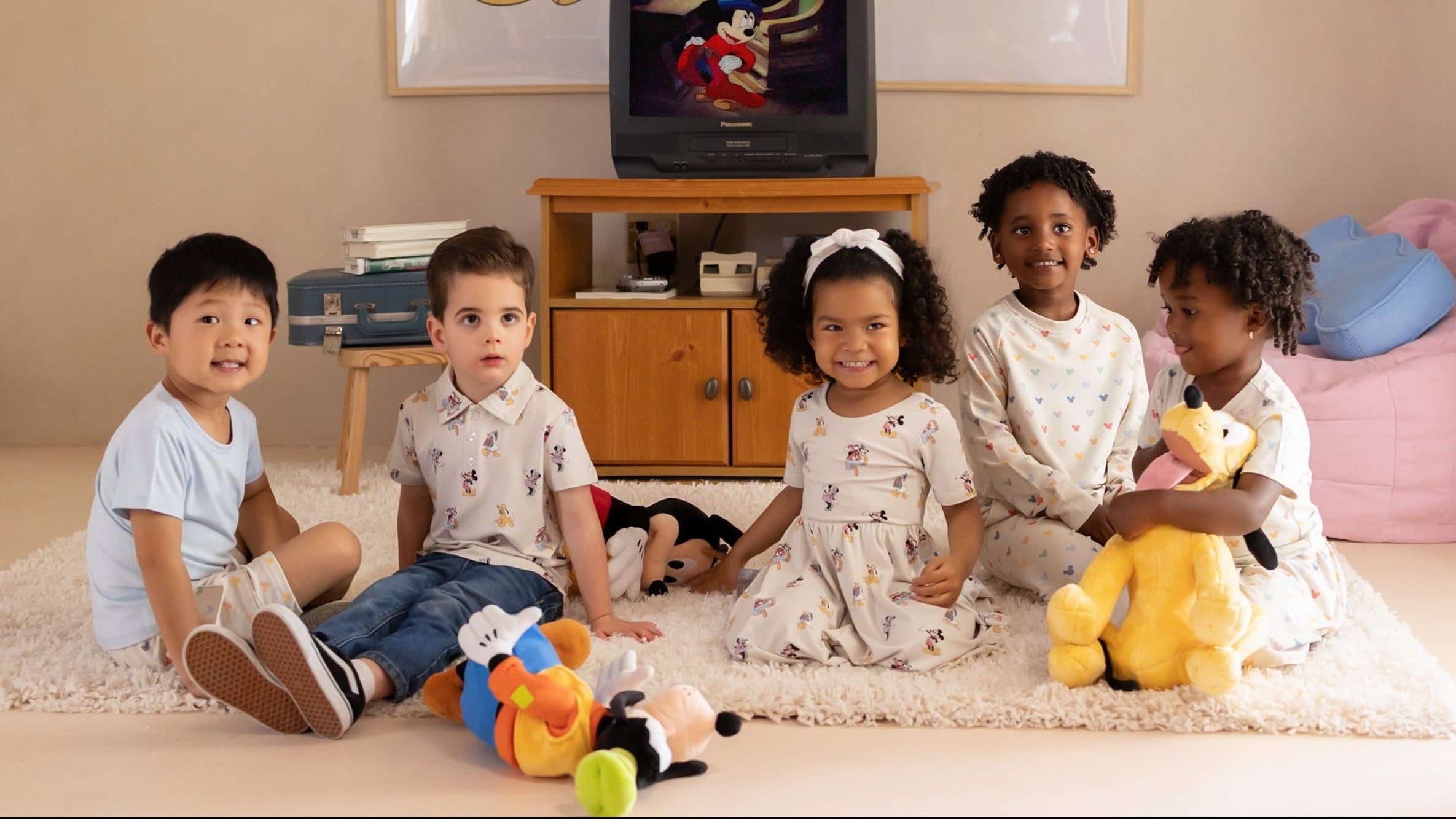 Group of children in a nostalgic room with bean bag chair and vintage TV wearing Disney x Kyte collection