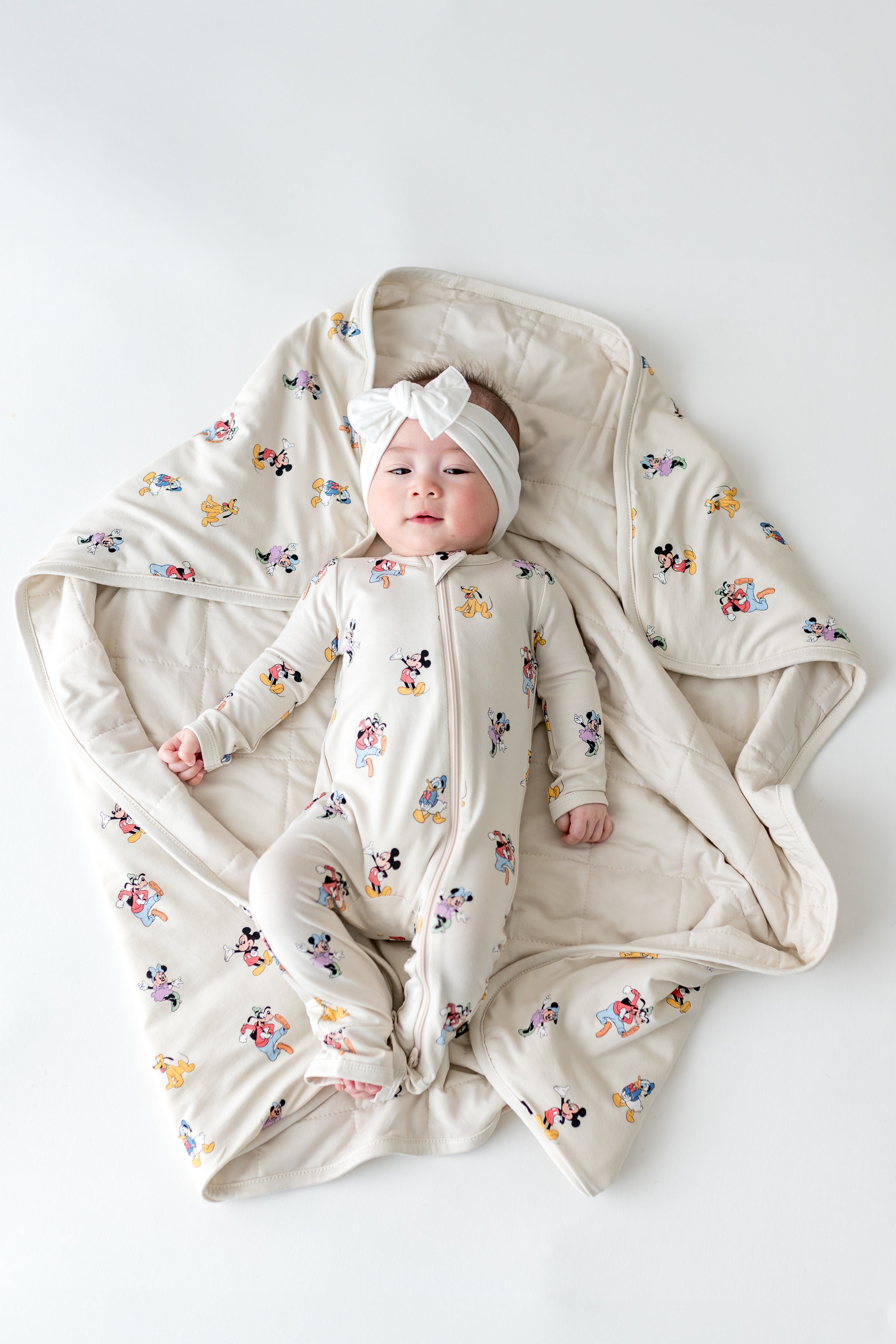 Baby wearing a Mickey Mouse footie laying on a matching baby blanket