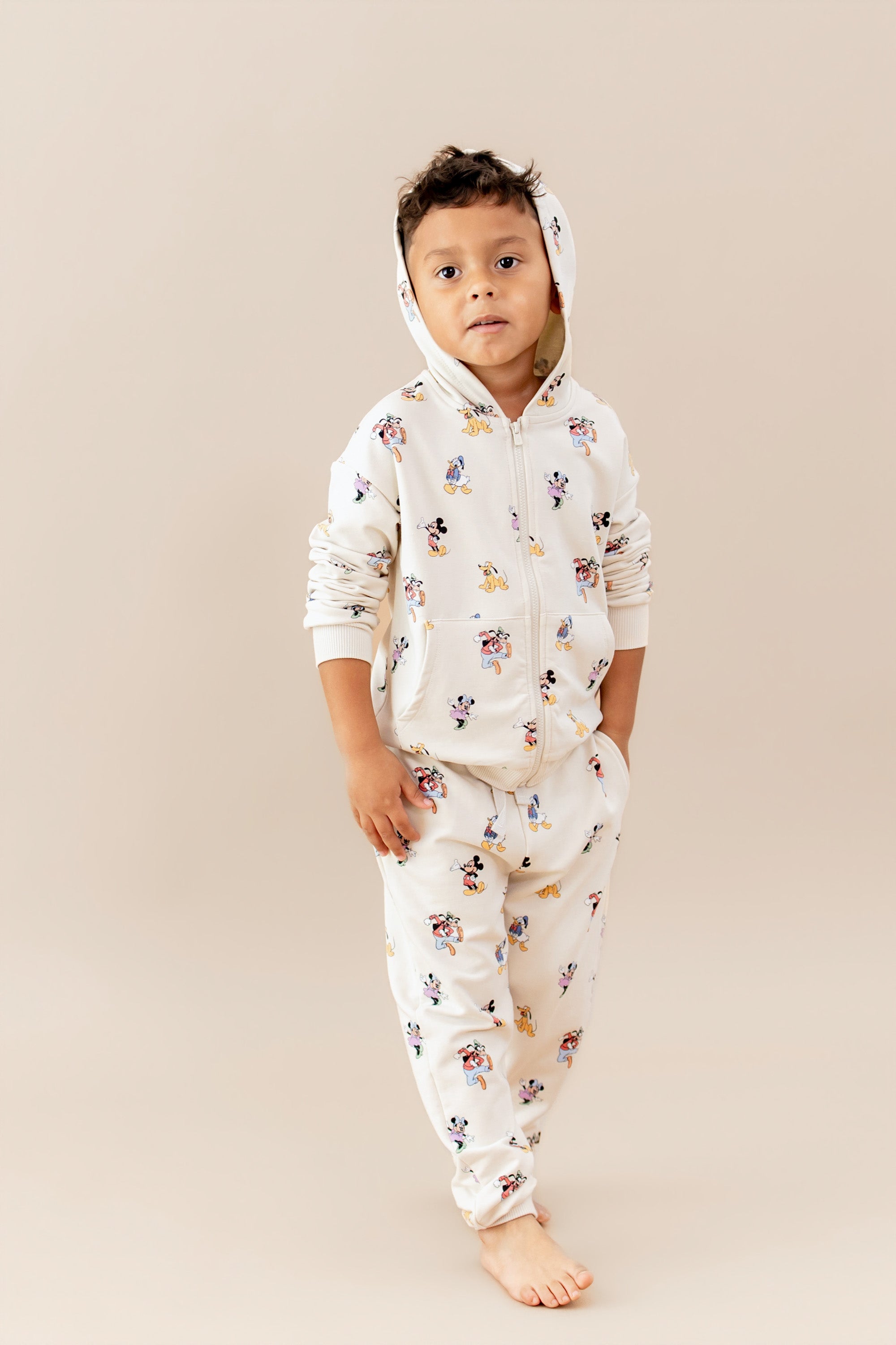 Child wearing a matching sweatsuit with a mickey and friends pattern featuring a zip up hoodie and jogger style pants