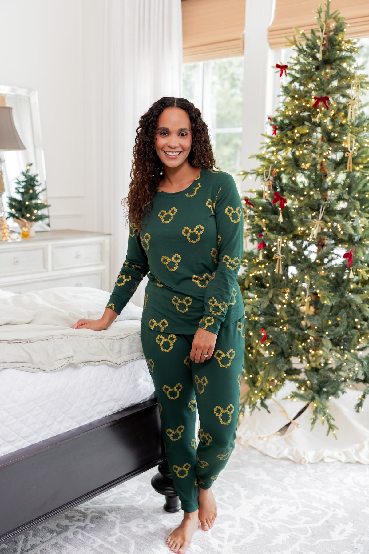 Woman wearing Women's Jogger Pajama Set in Mickey Christmas Wreath print standing in front of Christmas tree in a bedroom