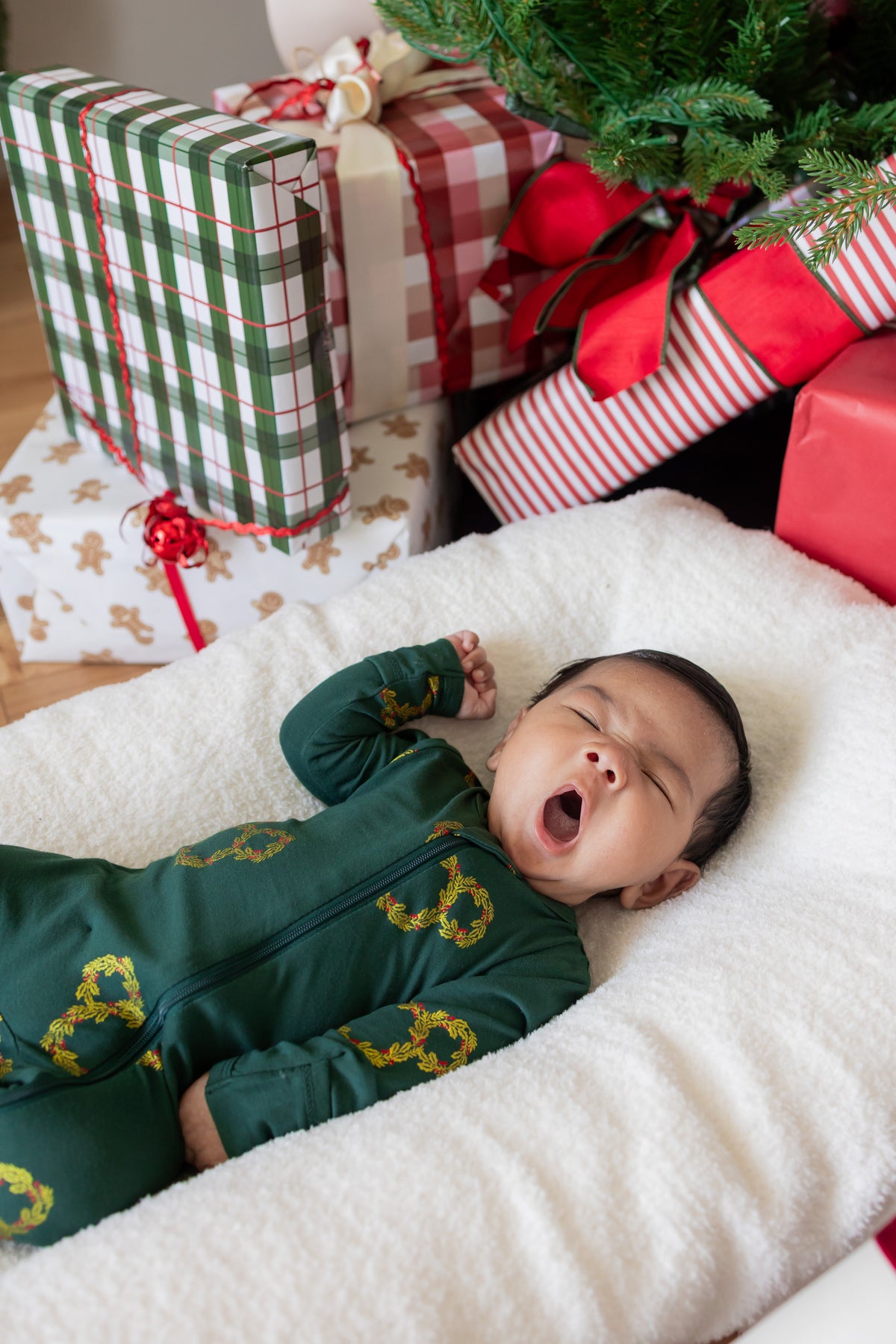 Baby yawning wearing Zippered Footie in Mickey Christmas Wreath print lying between presents