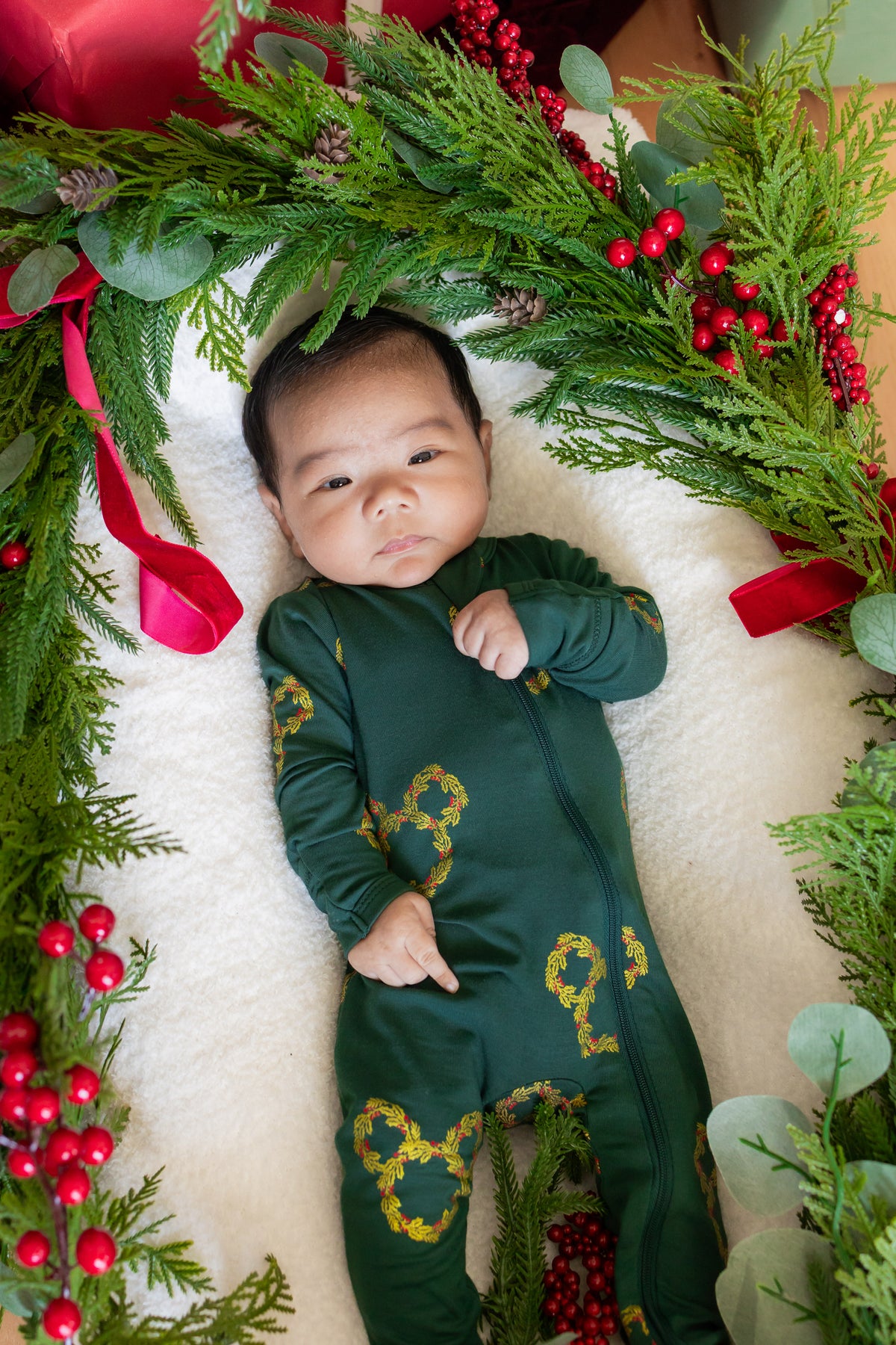 Baby wearing Zippered Footie in Mickey Christmas Wreath print lying between Christmas decorations