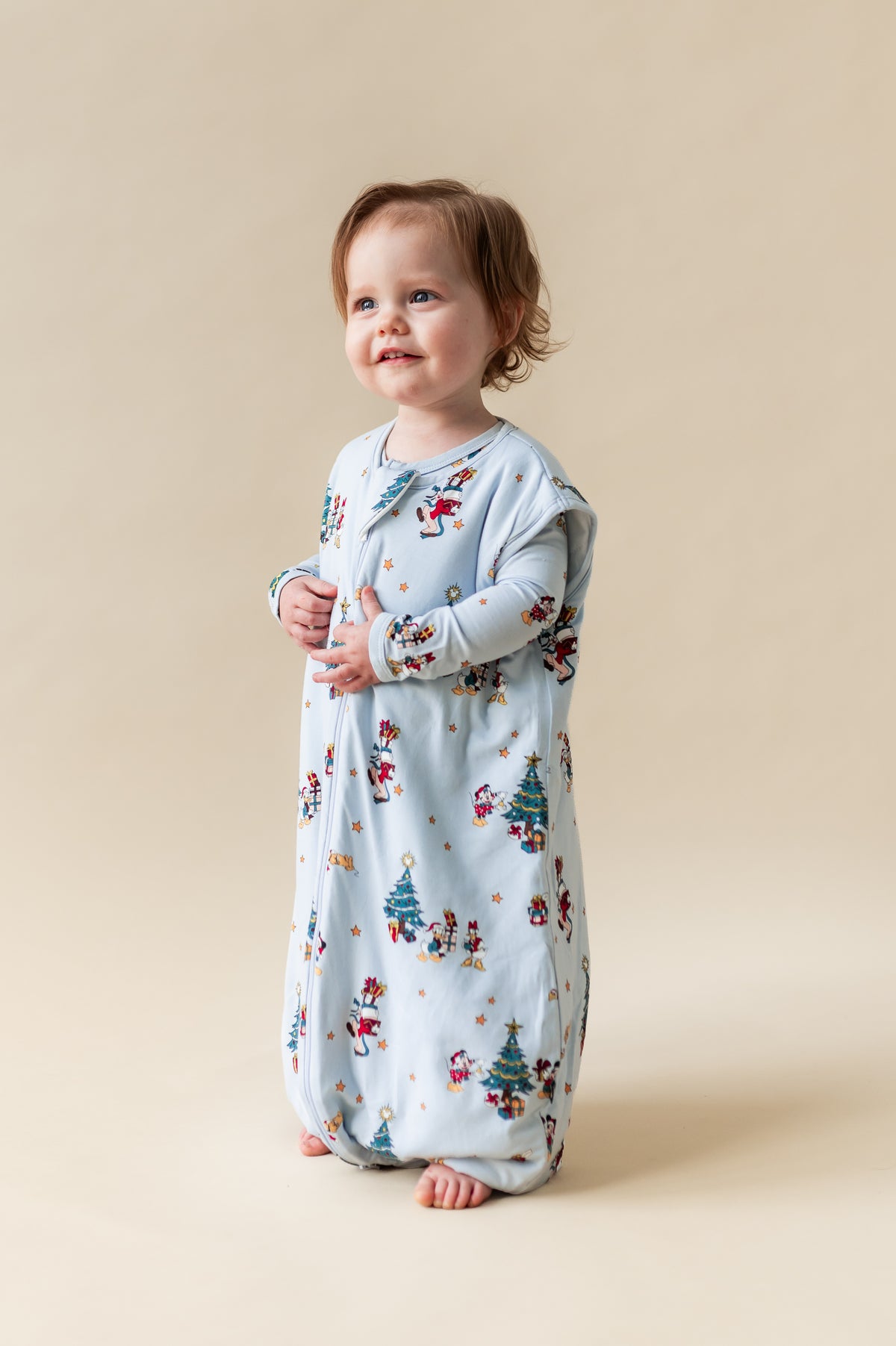 Toddler standing wearing Sleep Bag Walker in Mickey & Friends Christmas 1.0 print on a beige background