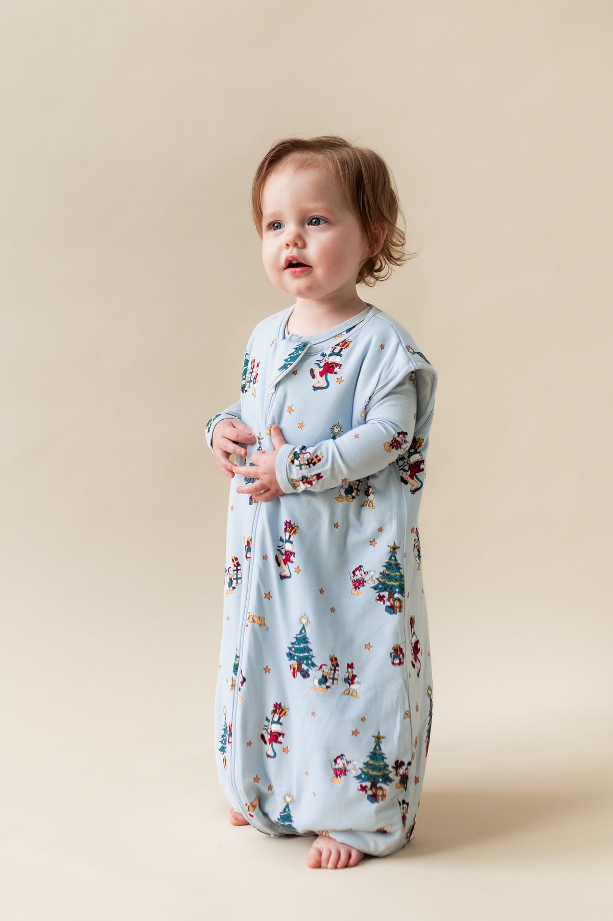 Toddler standing wearing Sleep Bag Walker in Mickey & Friends Christmas 1.0 print on a beige background