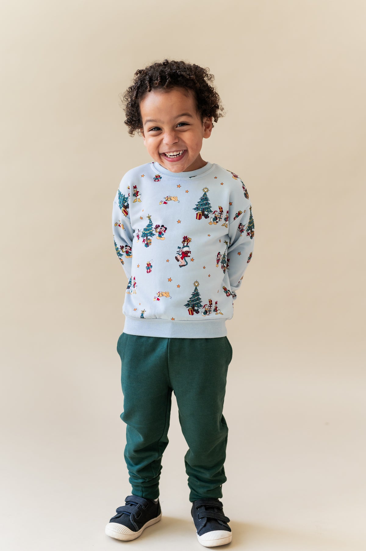 Boy posing in Sweatshirt in Mickey & Friends Christmas print over green pants