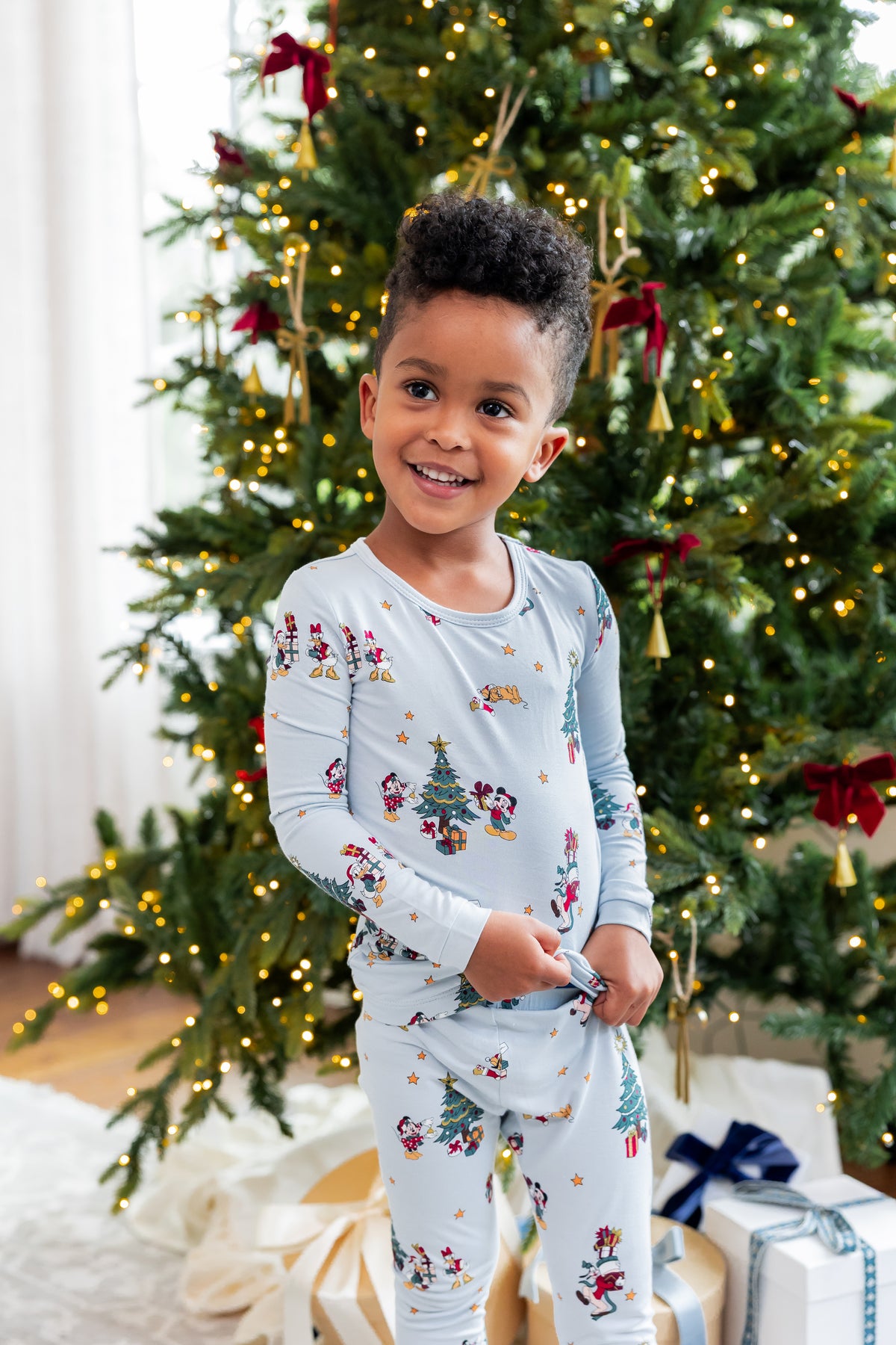 Boy standing in front of Christmas tree and presents wearing Long Sleeve Pajamas in Mickey & Friends Christmas print