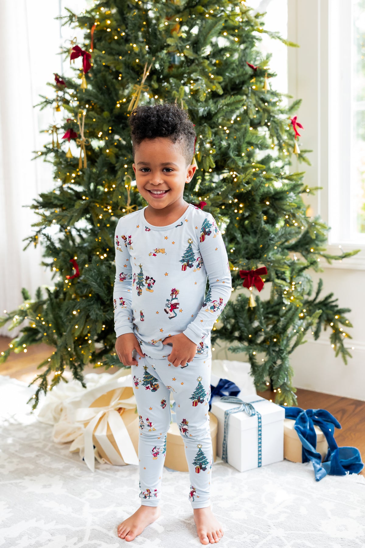 Boy standing in front of Christmas tree and presents wearing Long Sleeve Pajamas in Mickey & Friends Christmas print