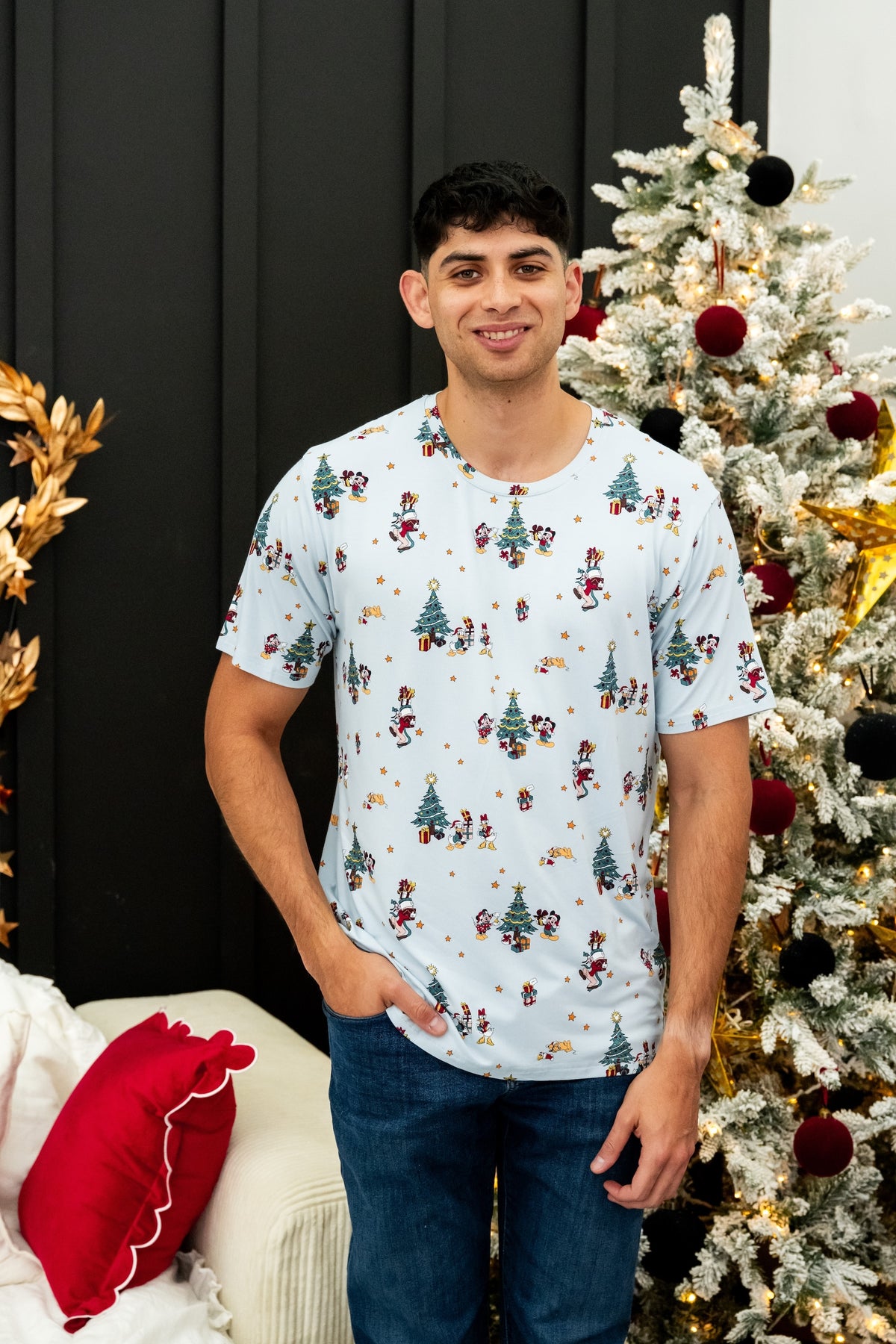 Modal wearing Men's Crew Neck Tee in Mickey & Friends Christmas print over dark blue jeans standing in front of Christmas tree