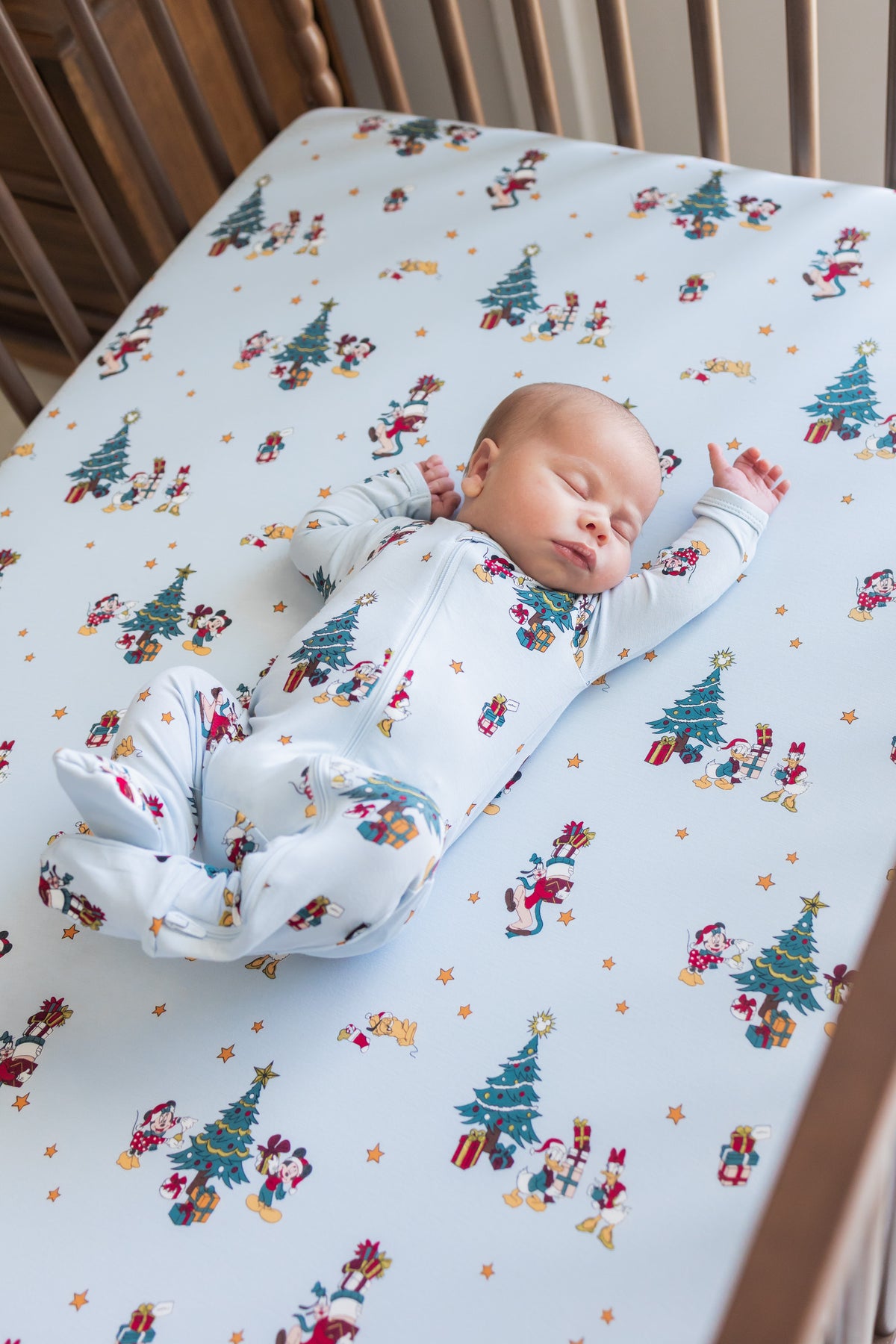 Baby sleeping in crib wearing Zippered Footie in Mickey & Friends Christmas print over similar print crib sheet