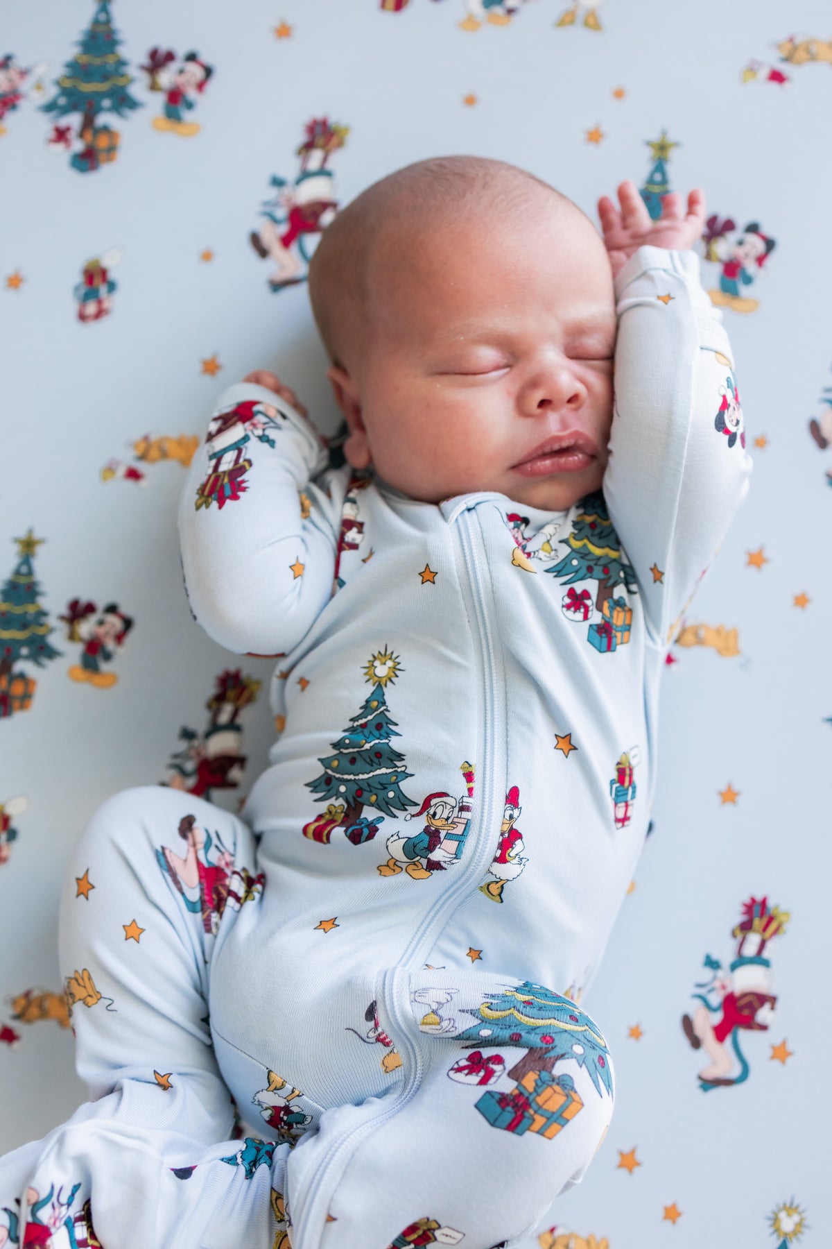 Baby sleeping while wearing Zippered Footie in Mickey & Friends Christmas print over similar print sheet