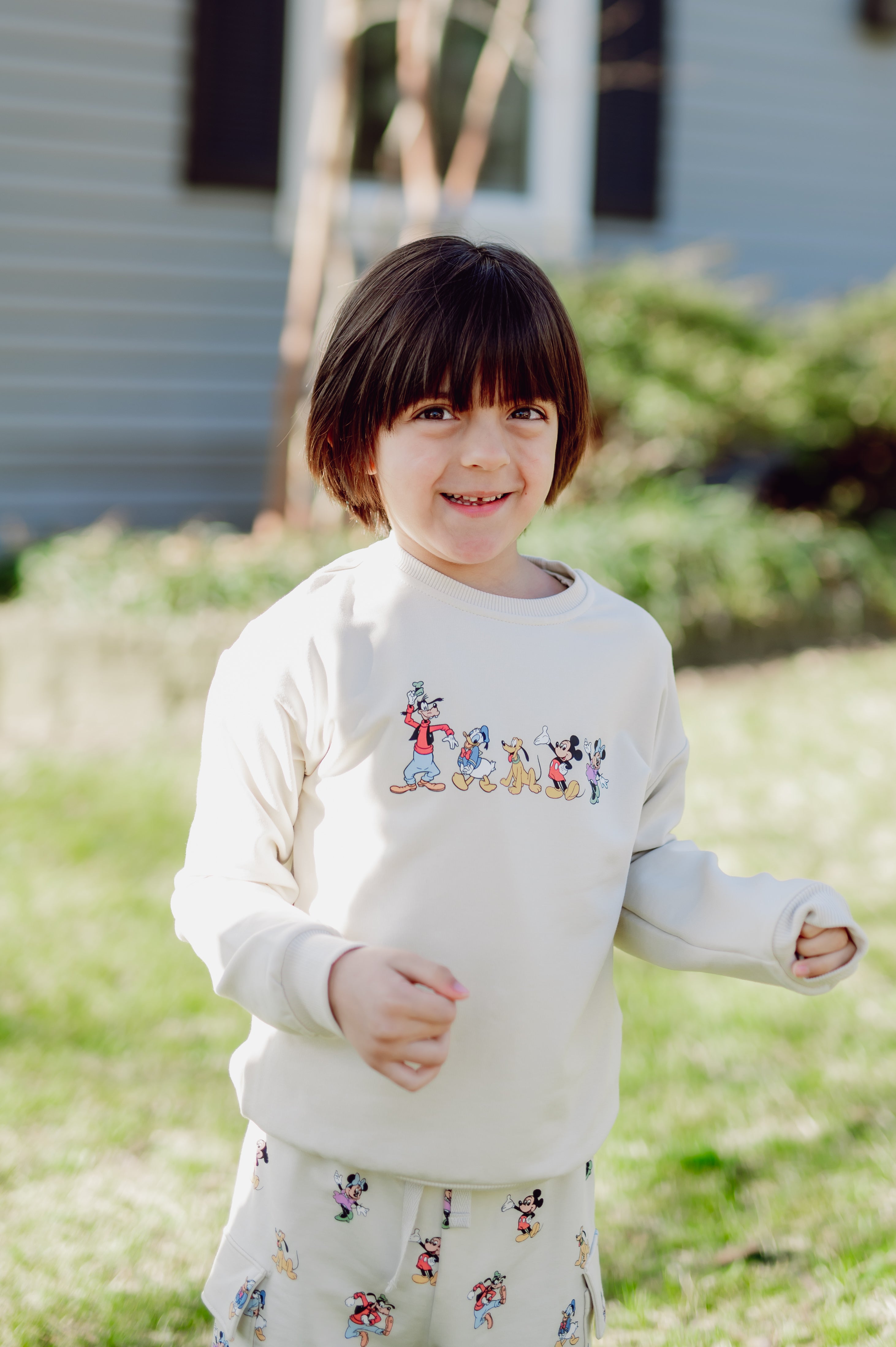 Child wearing a white sweatshirt with cartoon mickey character designs outdoors.