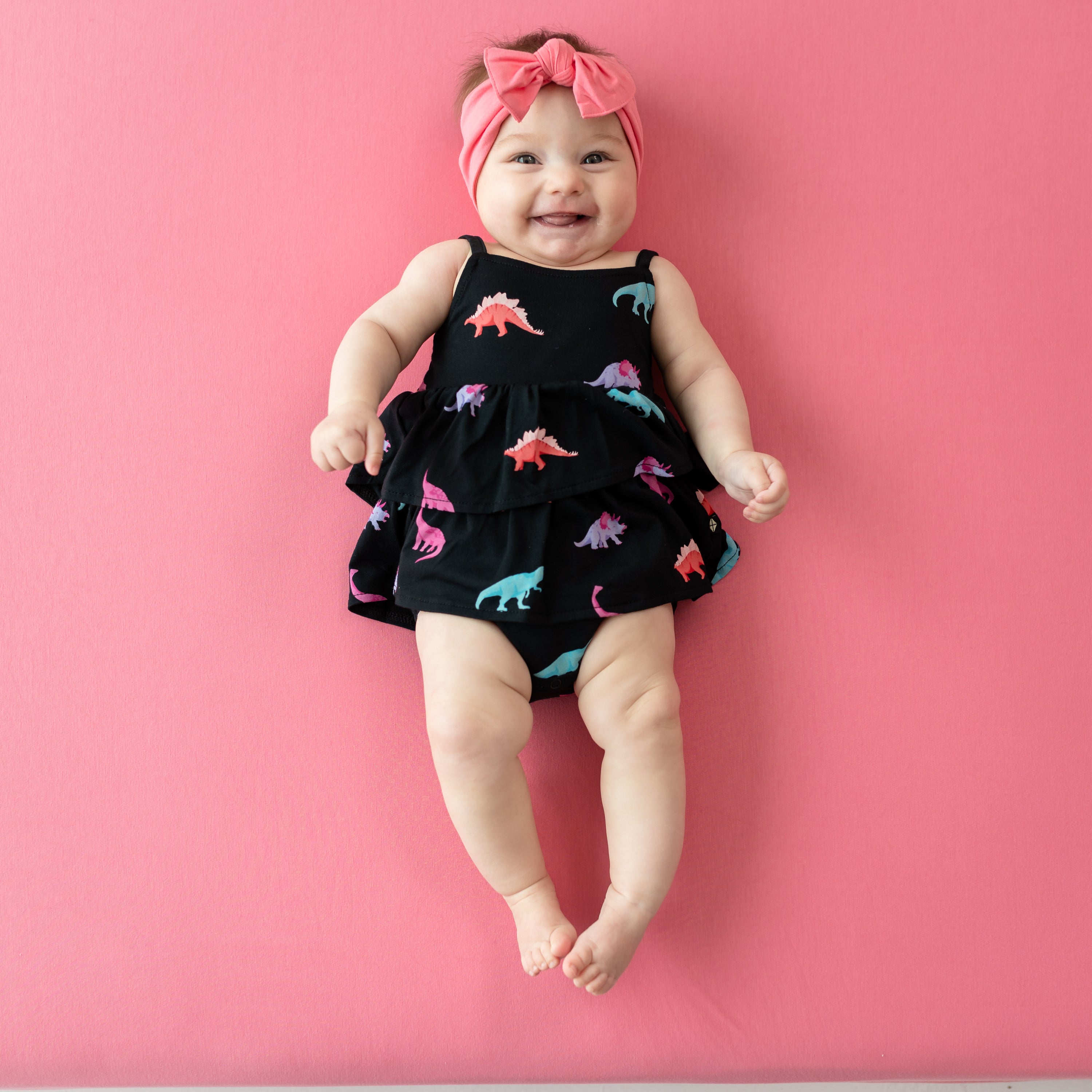 Smiling infant in Midnight Roar Spaghetti Strap Ruffle Romper with a Guava Bow