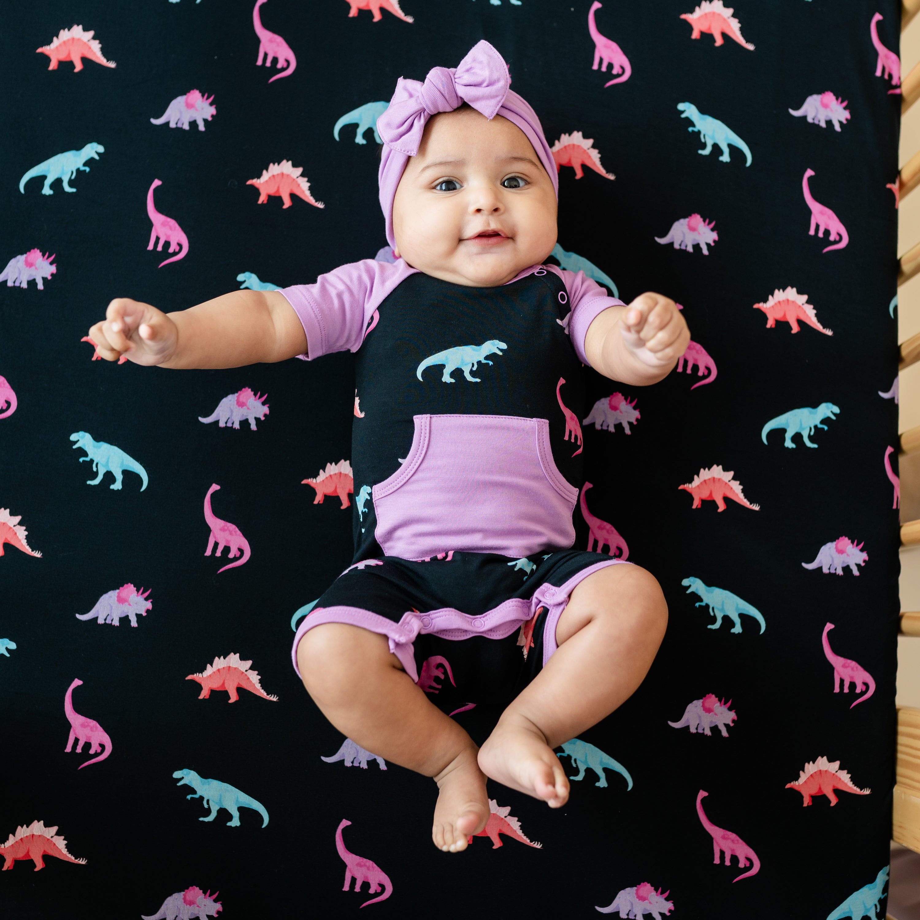 Infant model in Poi Bow and Midnight Roar Shortall that has a Poi trim and pocket color accent