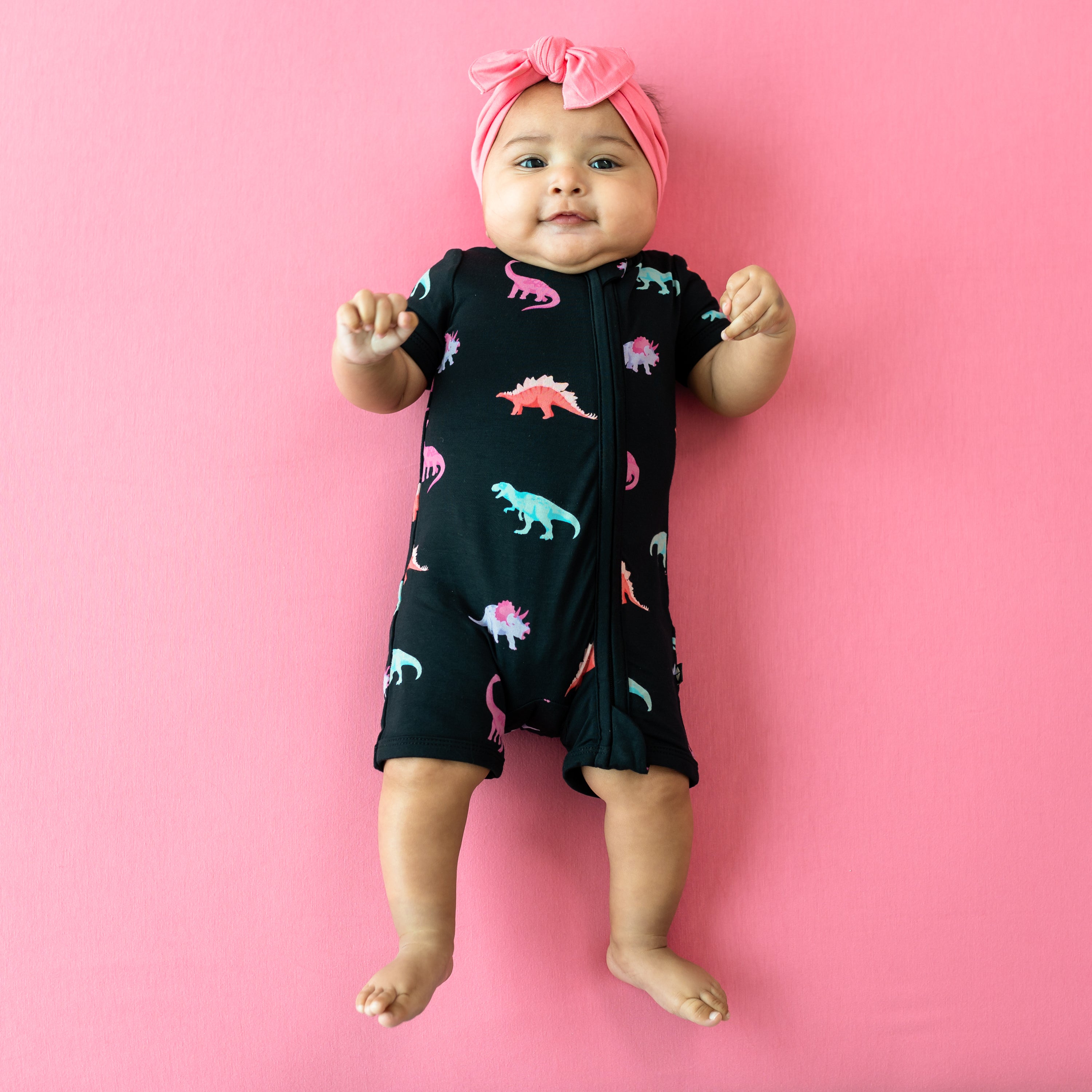 Infant modeling Kyte Baby Midnight Roar Zippered Shortall Romper with Guava Bow