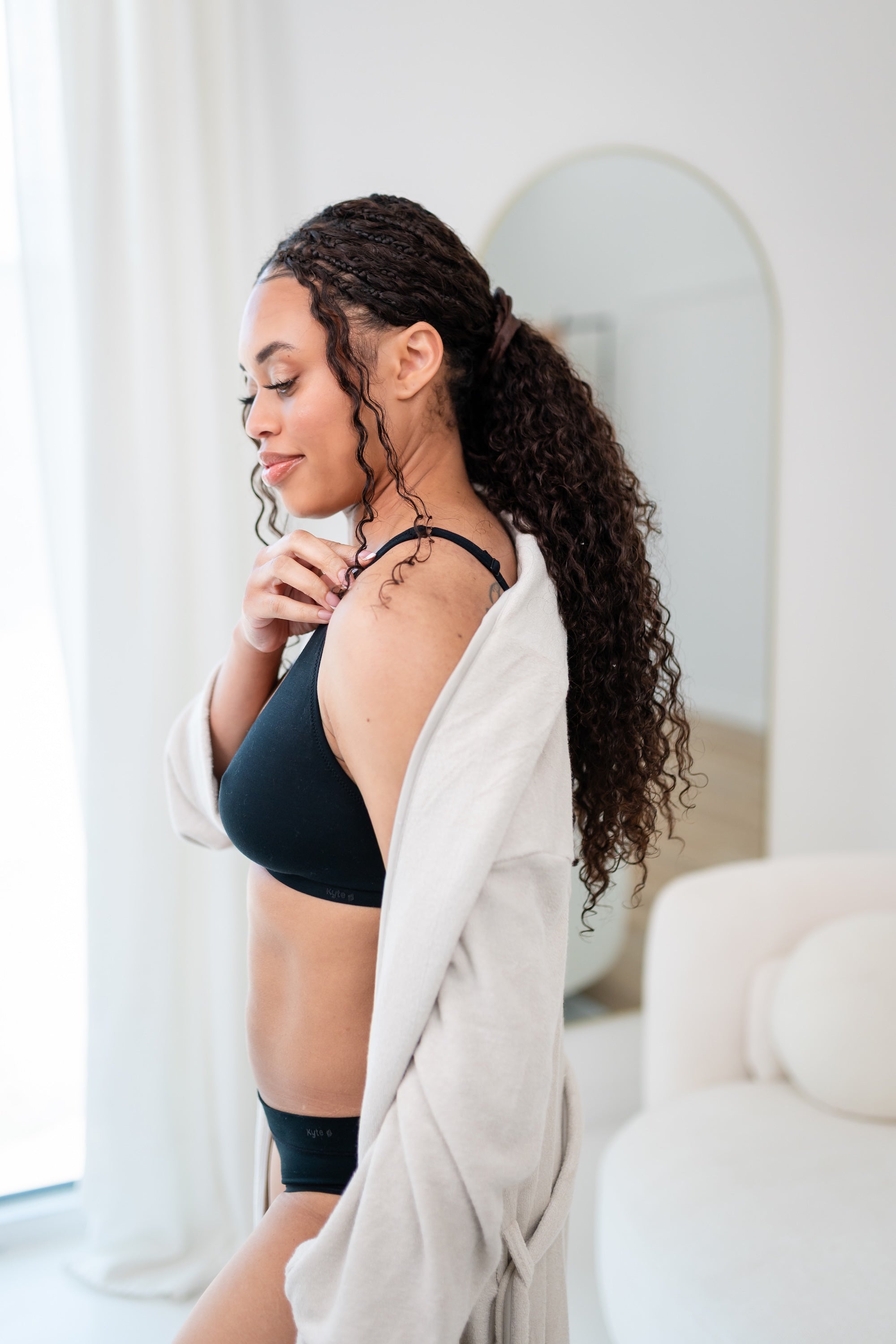 Woman wearing adjustable black cross front bralette and midi brief with oat cozy robe