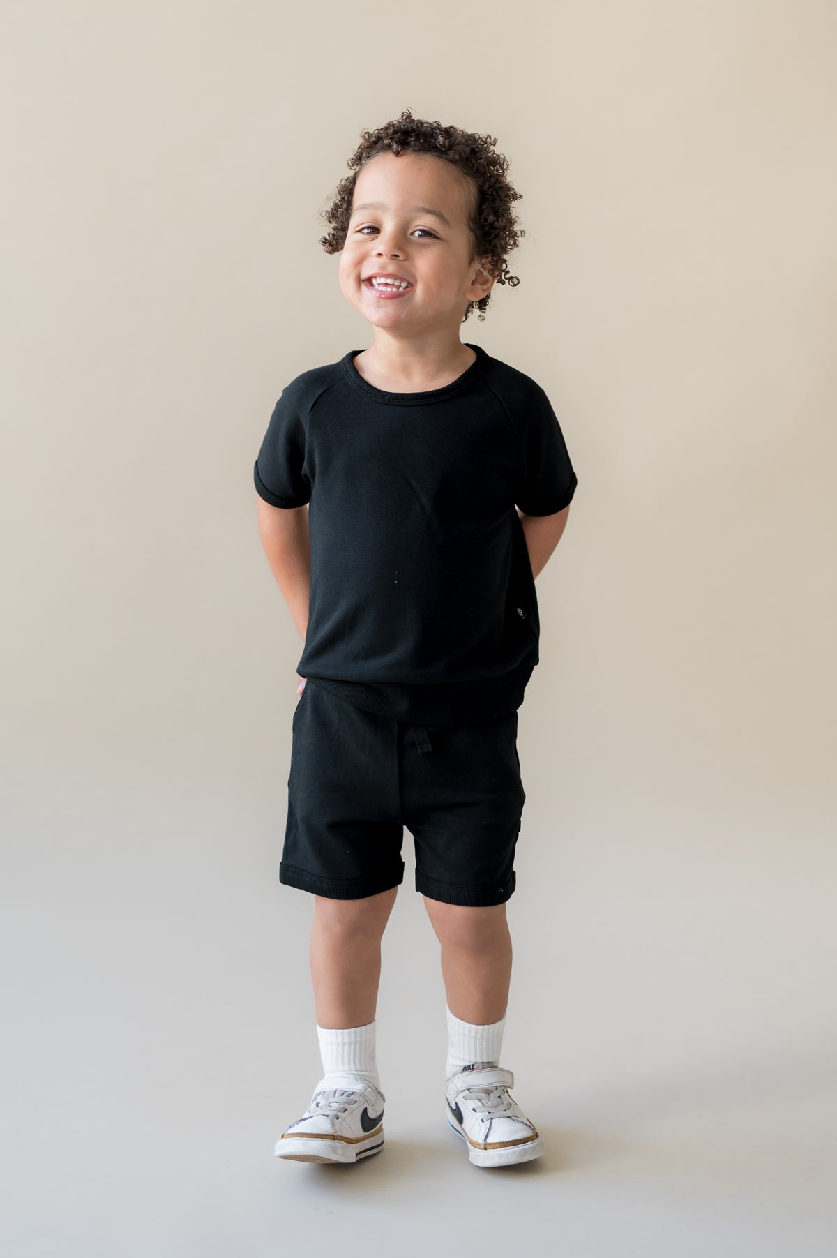 Young boy smiling with his hands behind his back wearing the Short Sleeve Jogger Set in Midnight