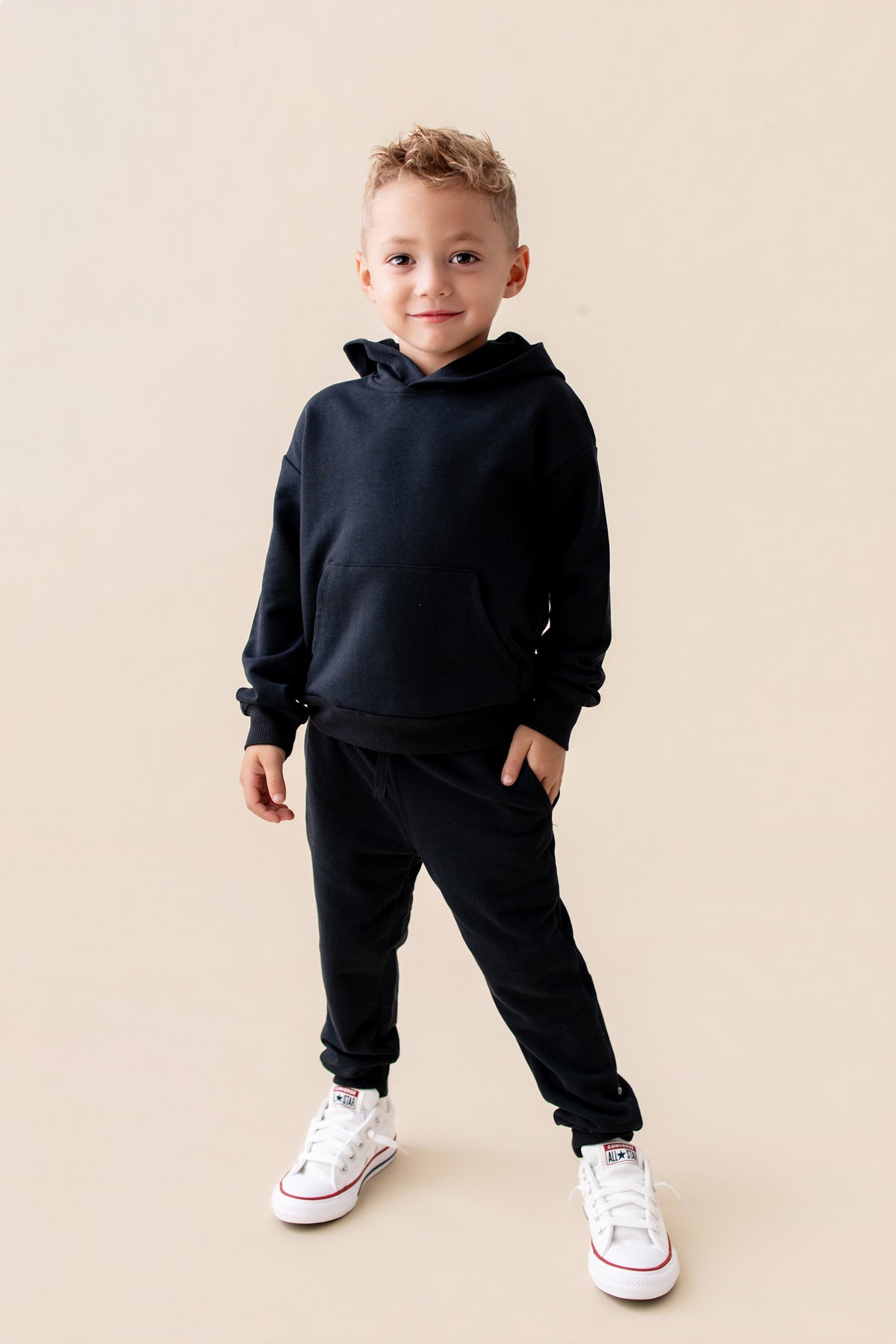 Boy wearing Jogger Pant in Midnight color under black hoodie with white shoes on a beige background