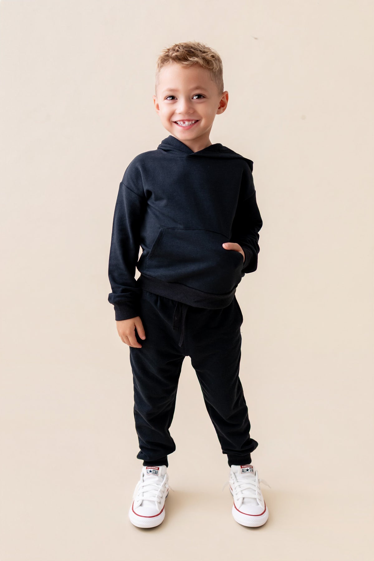 Boy wearing Hoodie in Midnight color over black jogger pants with white shoes on a beige background