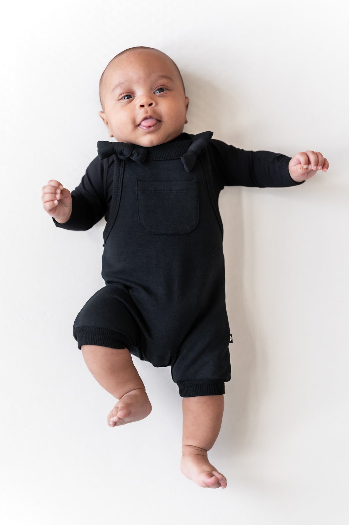 Baby wearing Overall in Midnight color lying on a beige background
