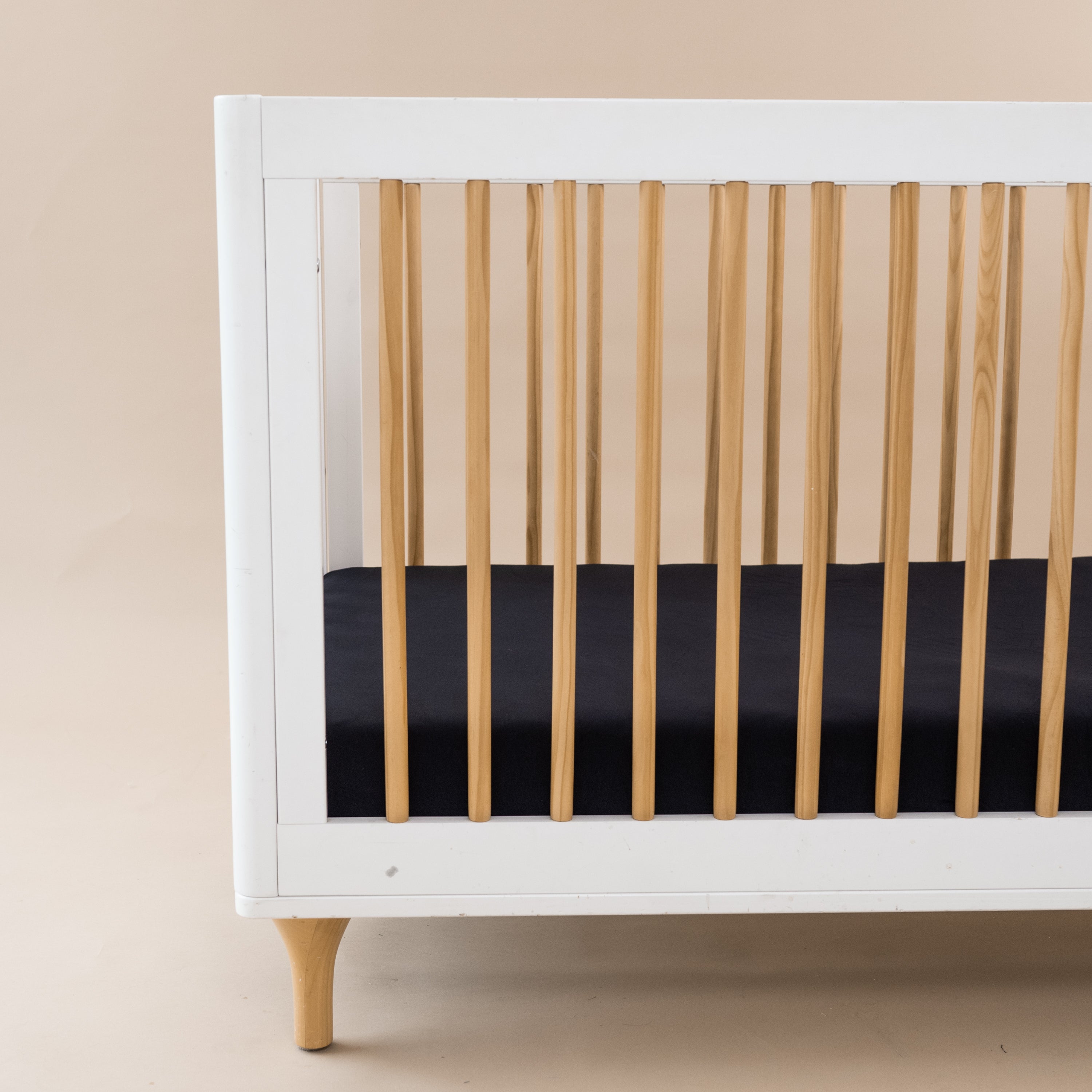 Crib Sheet in Midnight shown on a mattress in a modern white and wooden crib