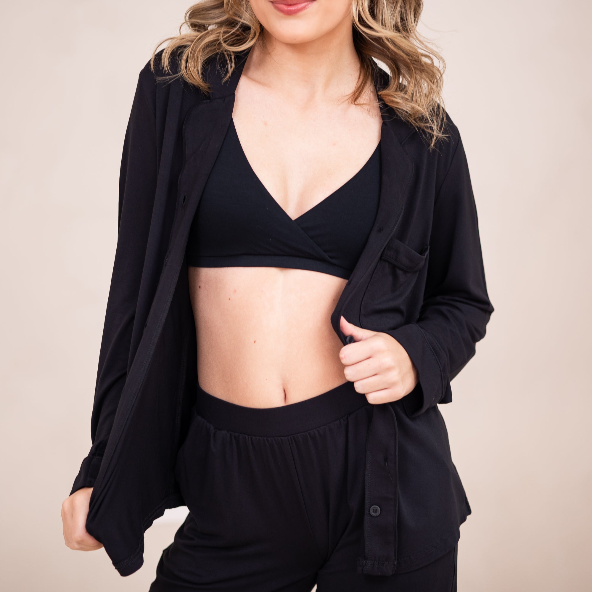 Female wearing the Women's Cross Front Bralette in Midnight underneath the Women's long sleeve pajama set in midnight unbuttoned