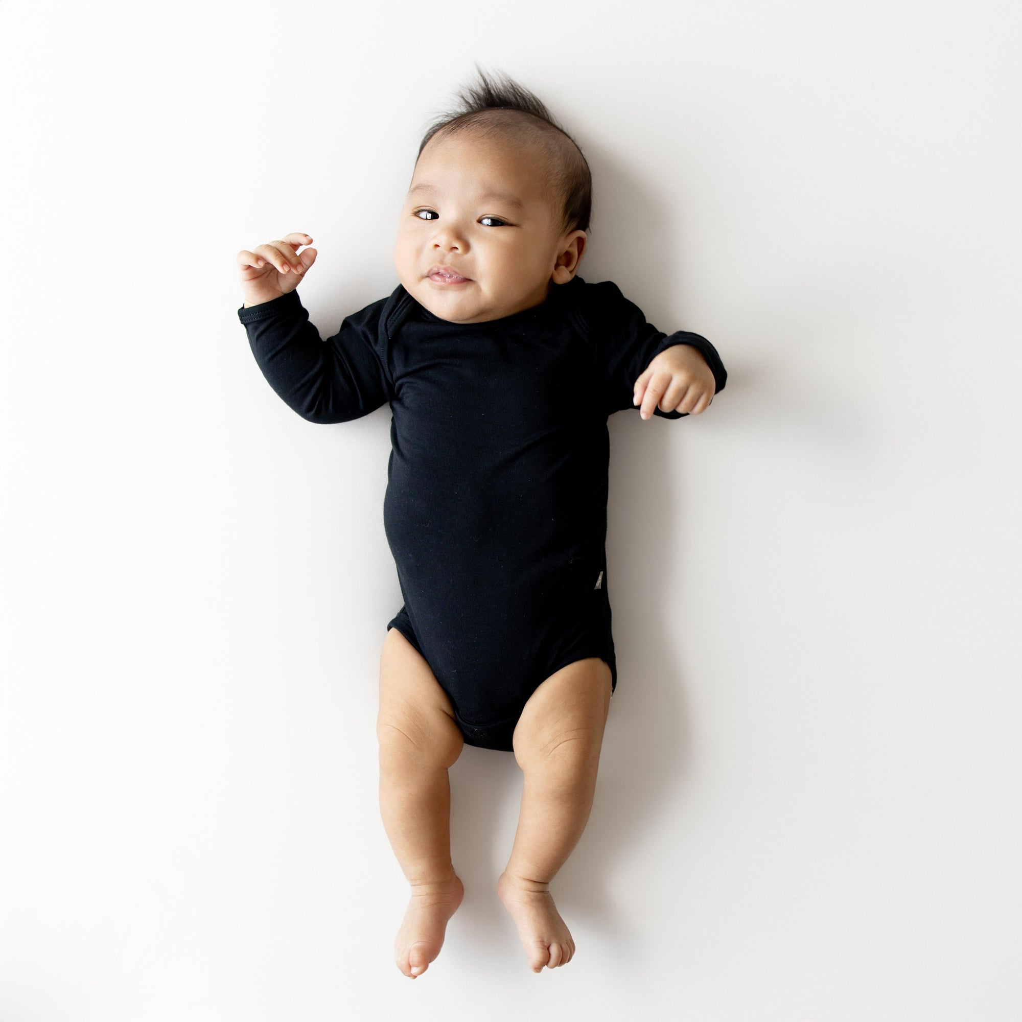 Baby in black long sleeve bodysuit on white surface
