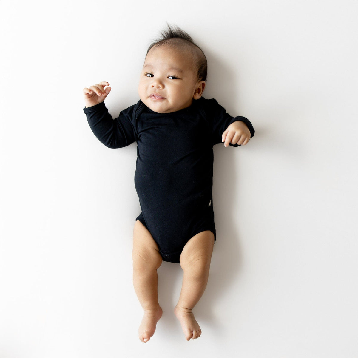 Baby in black long sleeve bodysuit on white surface