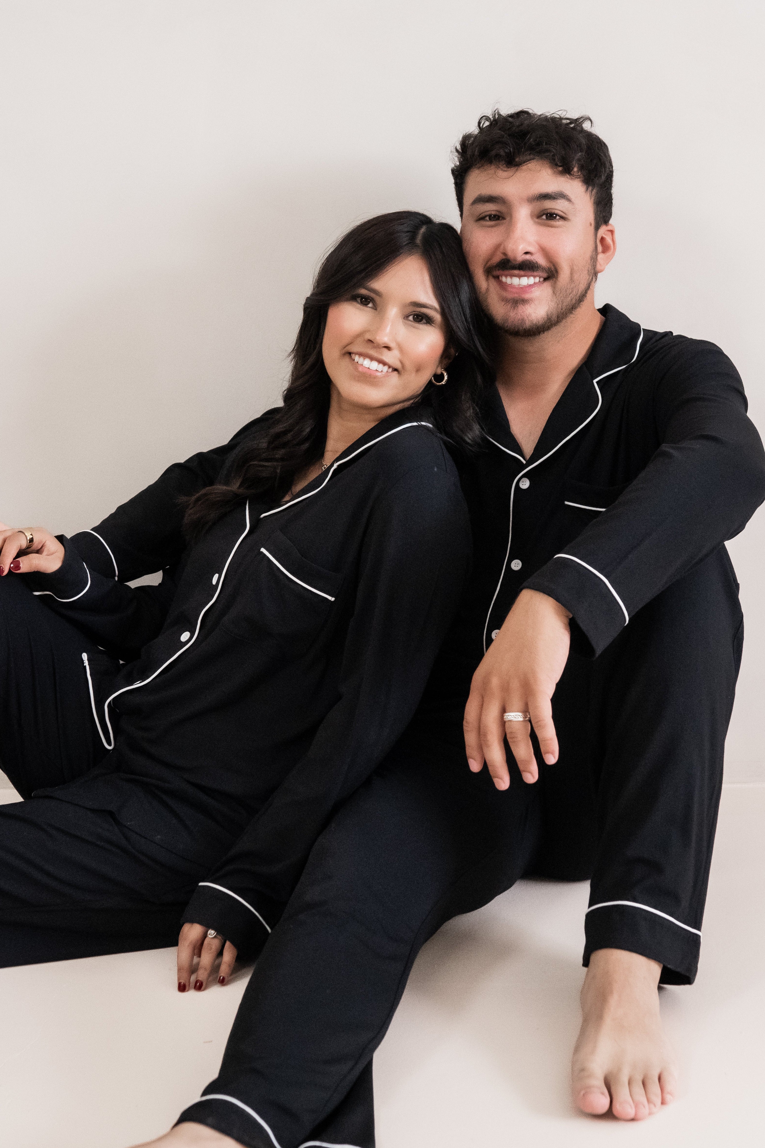Husand and wife sitting on the floor wearing matching Long sleeve Pajama Set in Midnight with Cloud Trim