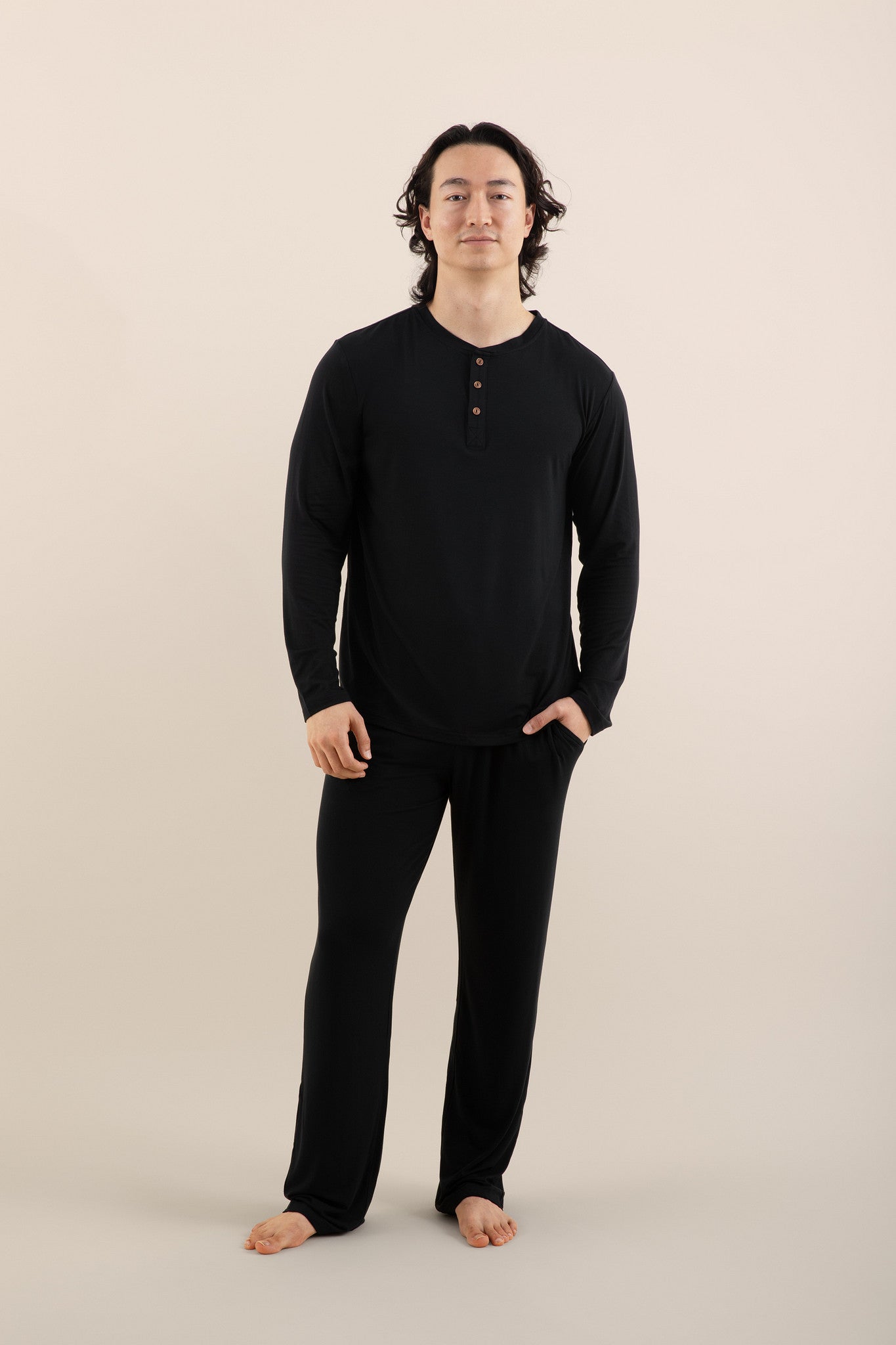 Male model wearing the Men's Long Sleeve Henley Top in Midnight and matching men's lounge pants with one hand in the pants pocket