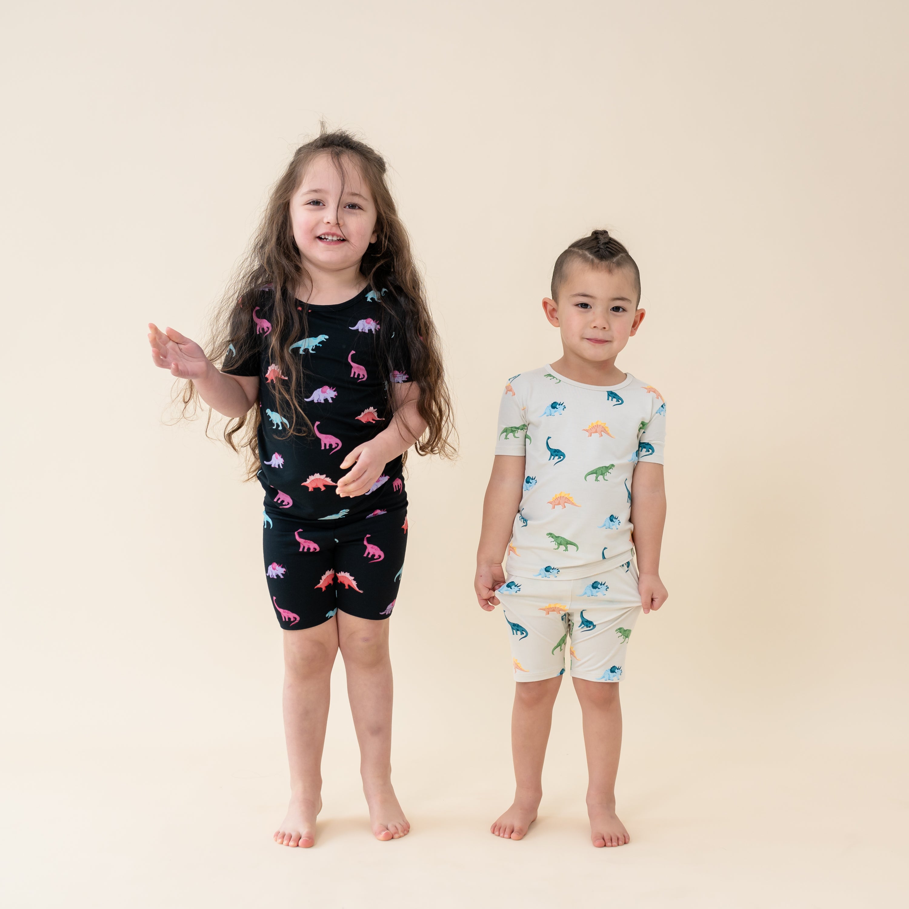 Two children wearing Short Sleeve Pajama Set in both Midnight and Ecru Roar Dinosaur print