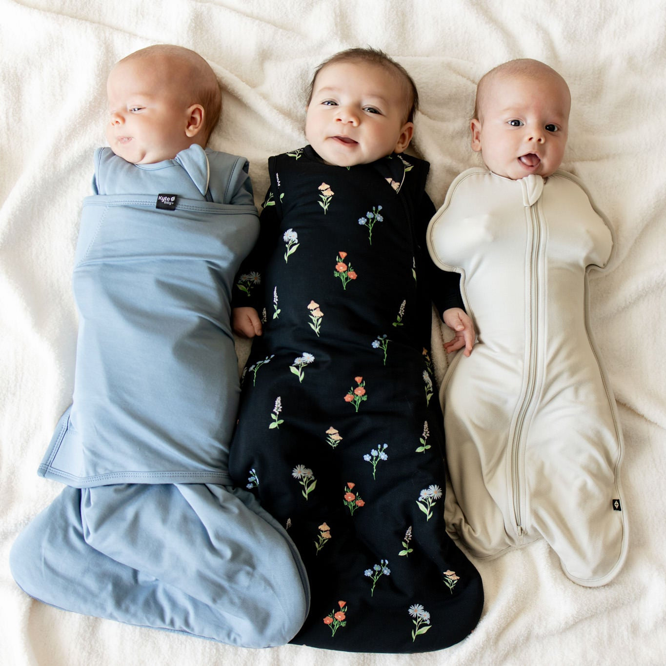 3 babies is different sleep sacks and swaddles on a soft cream blanket