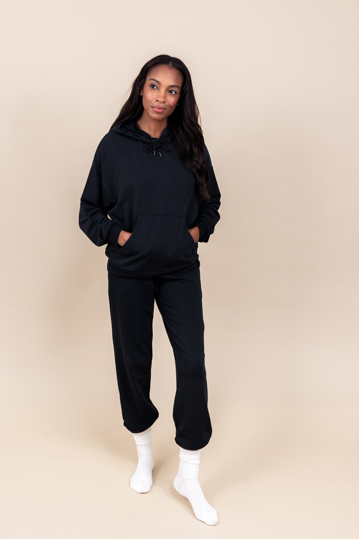 Woman wearing Women's Jogger Pants in Midnight color and a similar color Hoodie on a beige background