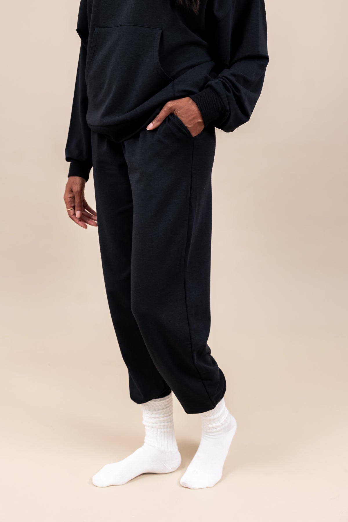 Woman wearing Women's Jogger Pants in Midnight color and a similar color Hoodie on a beige background