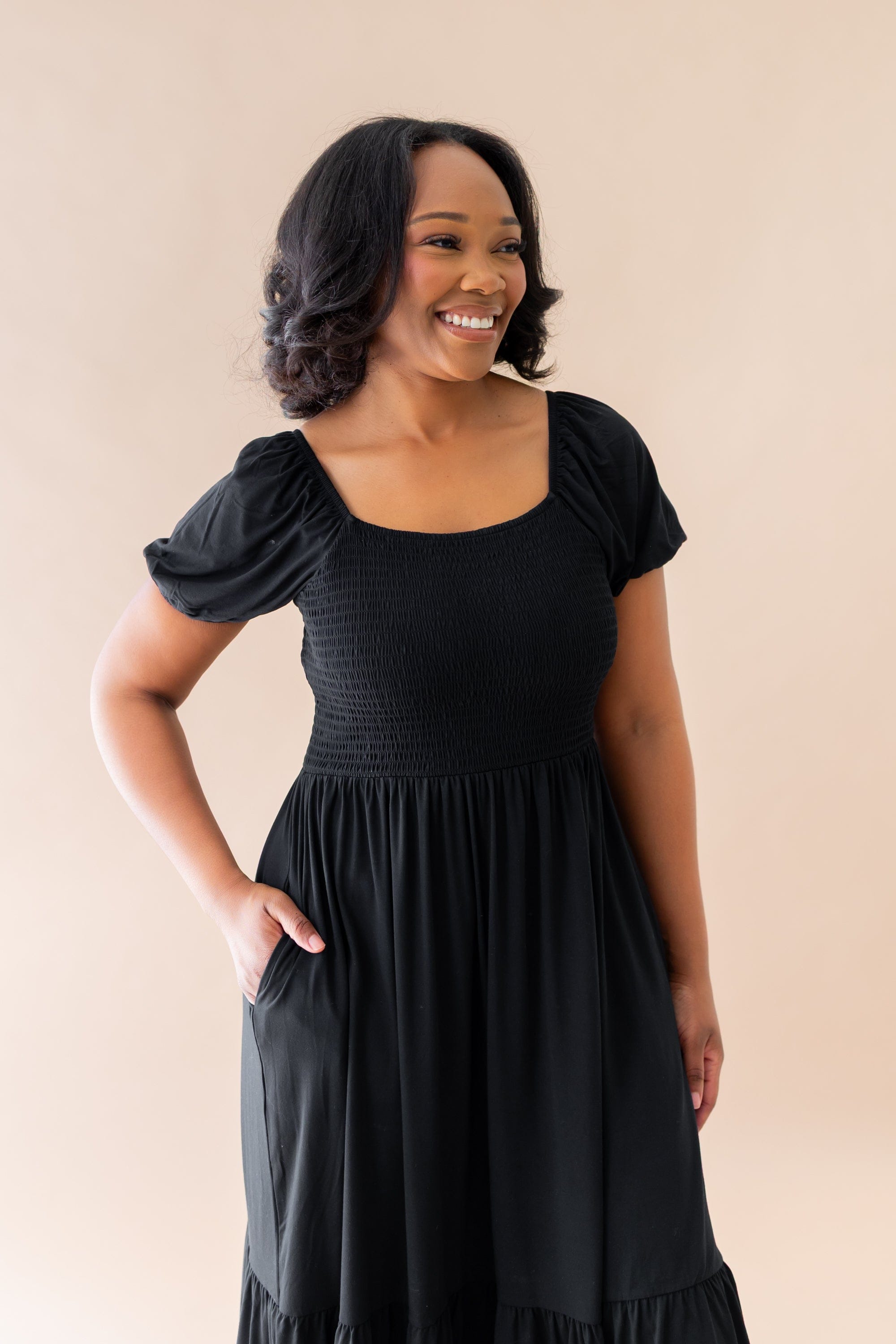 Smiling female wearing the Women’s Smocked Dress in Midnight with one hand in the dress pocket