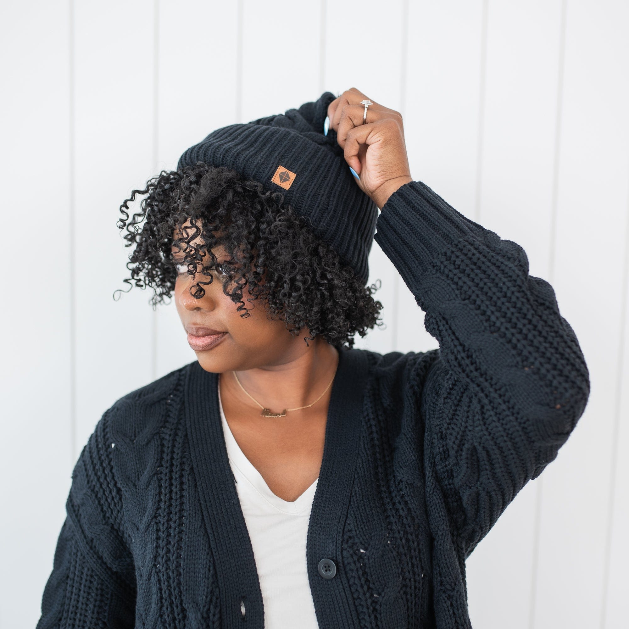 A model standing wearing the Cable Knit Adult Pom Beanie in Midnight with one hand on the top of the beanie