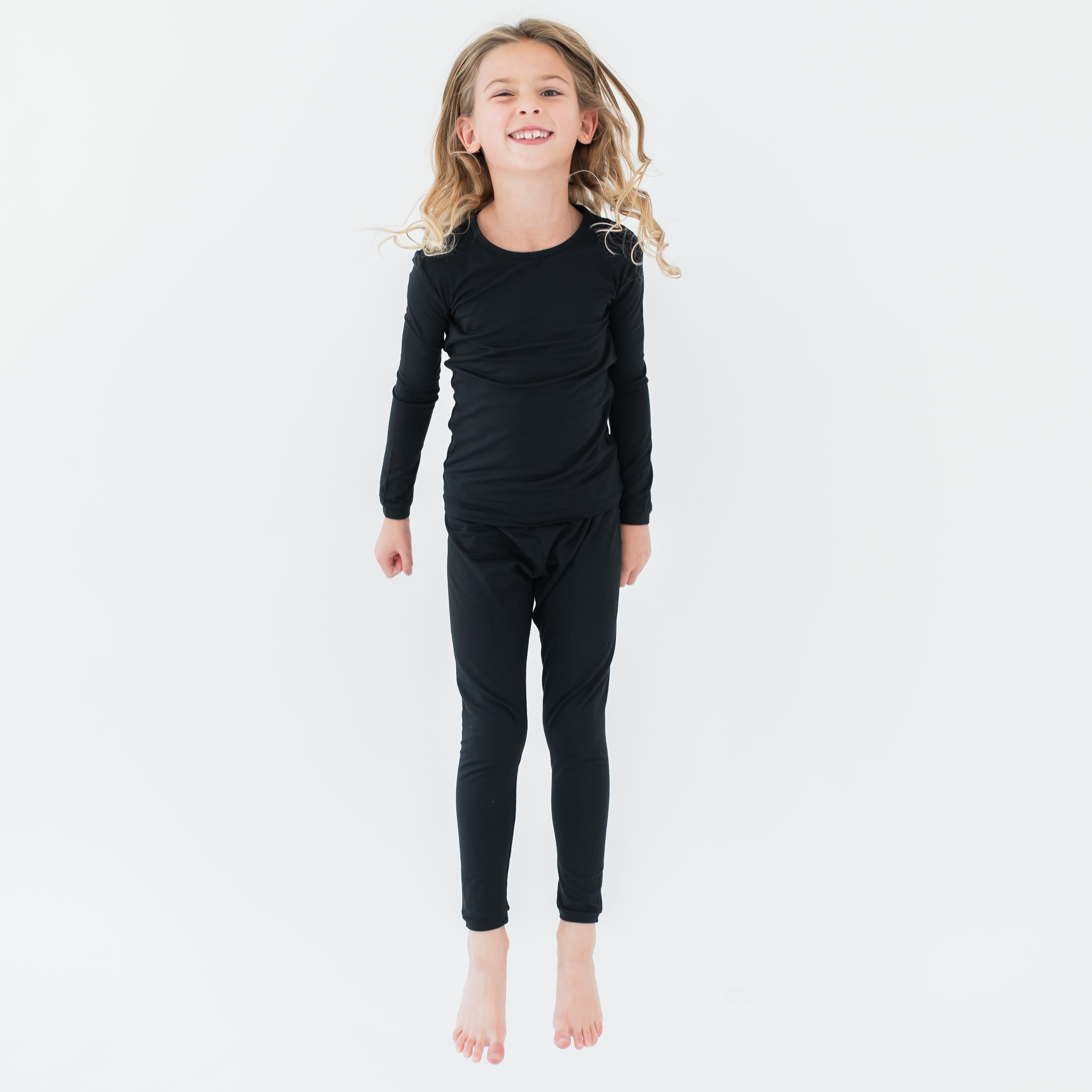 Young girl jumping in the air wearing the Long Sleeve Pajamas in Midnight in front of a white background