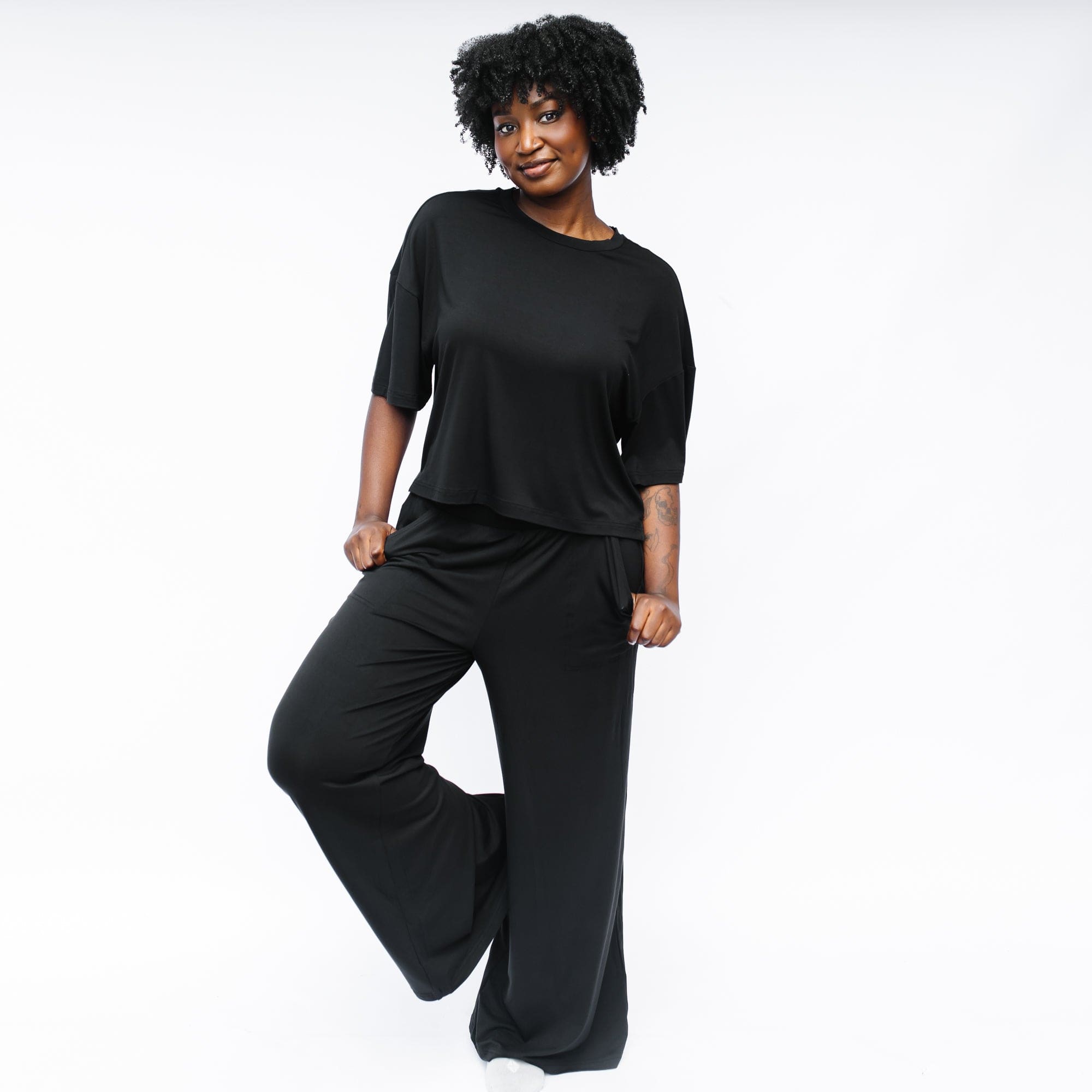 Female model standing in front of a white background wearing the Women's Short Sleeve Tee in Midnight with wide leg pants