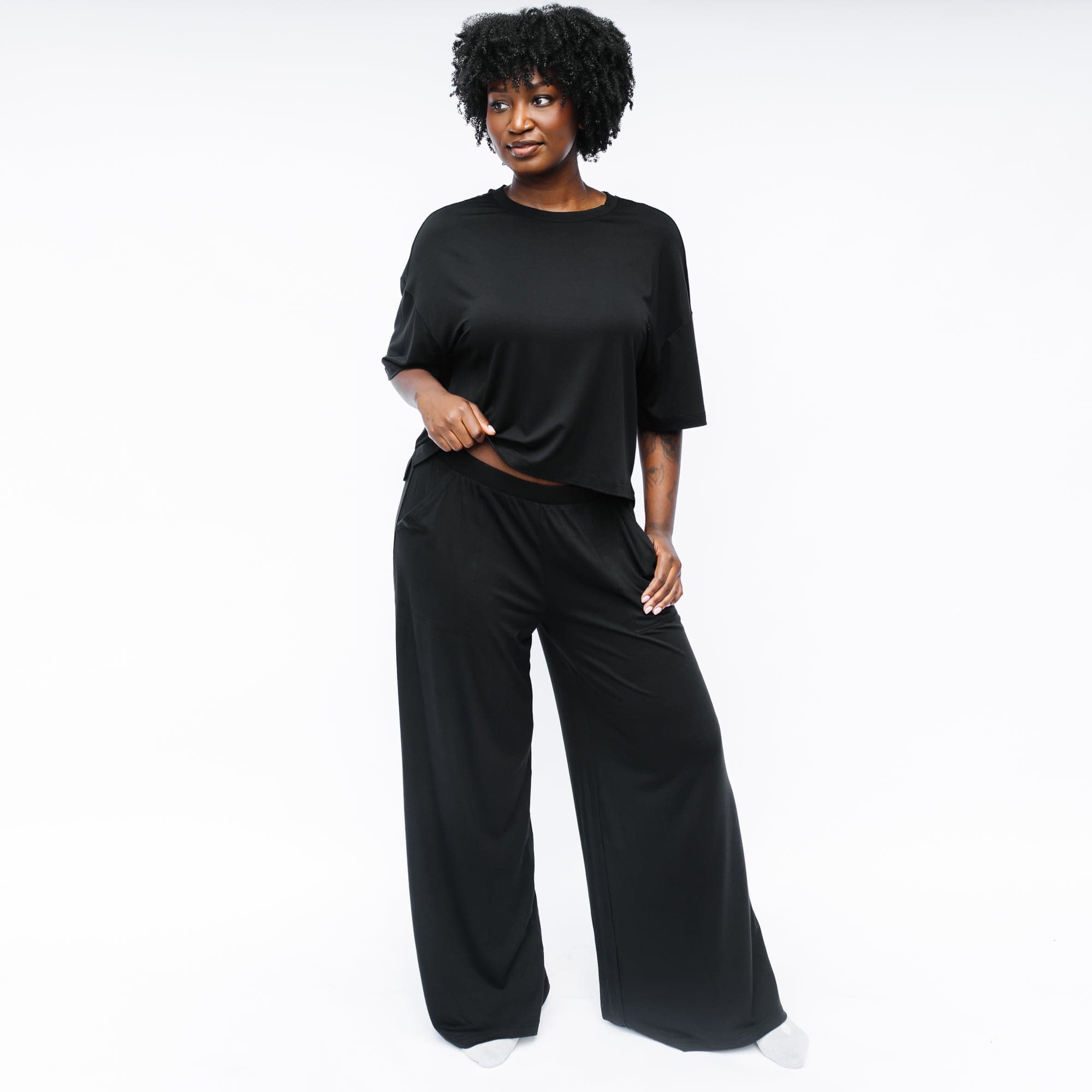 Female model standing in front off a white background looking off to the side wearing the Women's Wide Leg Pant in Midnight with matching women's short sleeve tee