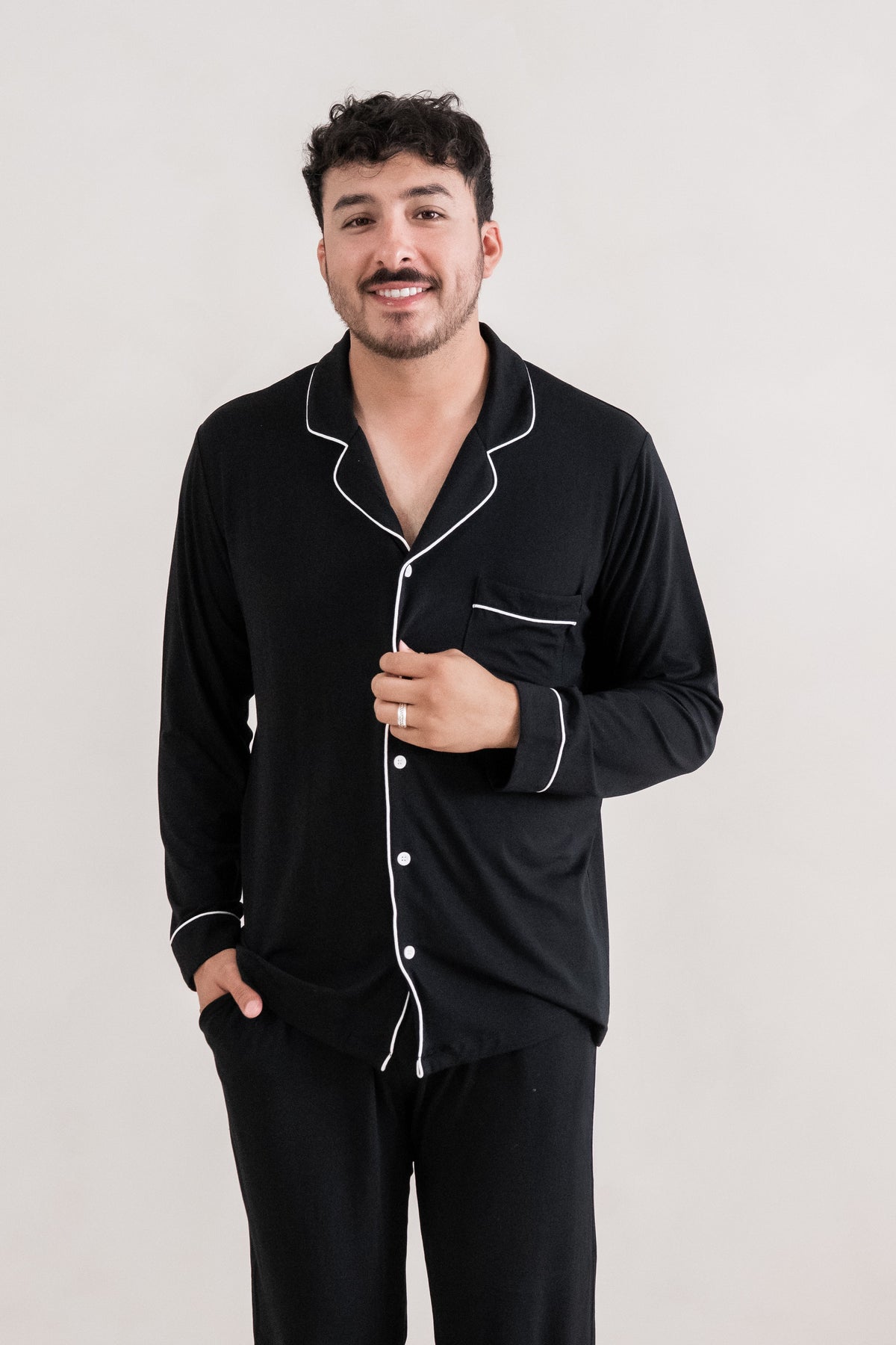 Close up of male model wearing the Men's Long Sleeve Pajama Set in Midnight with one hand on the buttons of the shirt and the other in the pants pocket