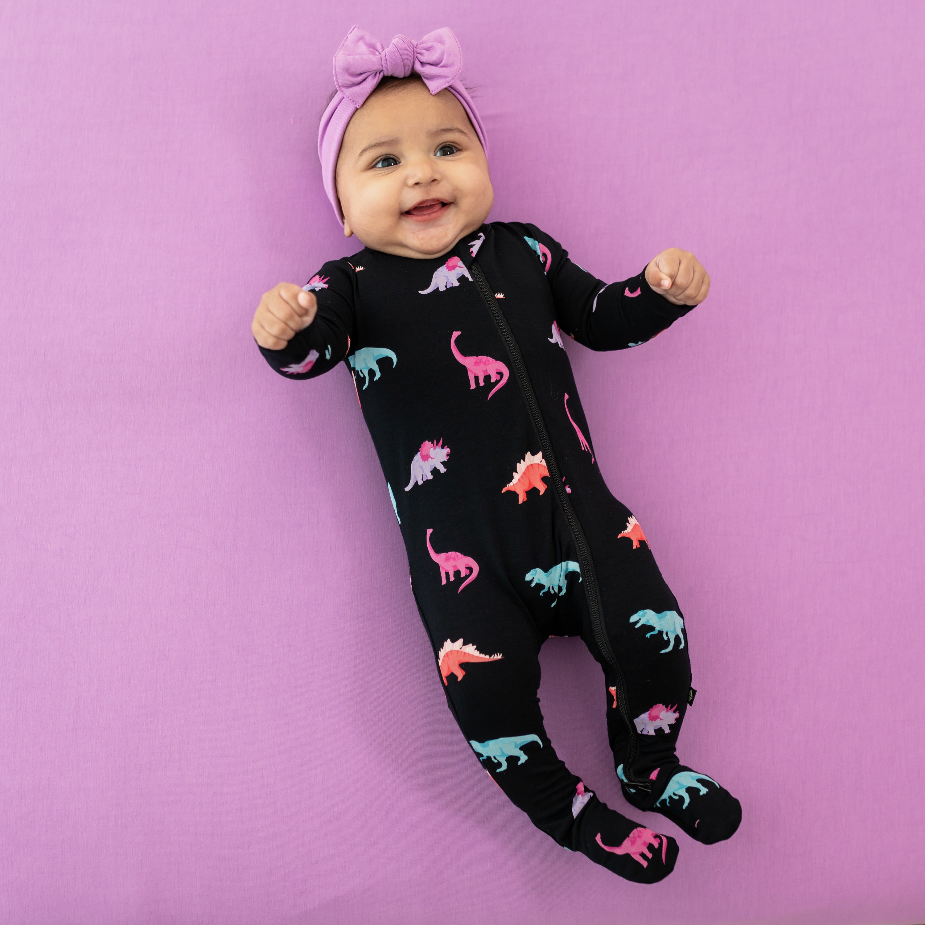 Infant shown in Midnight Roar zippered footie paired with a Poi bow