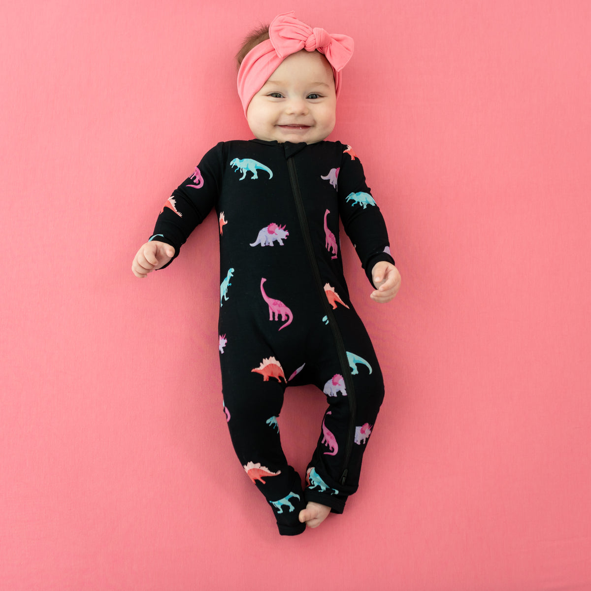 Smiling baby in Midnight Roar Zippered Romper paired with Guava Bow on Guava Blanket