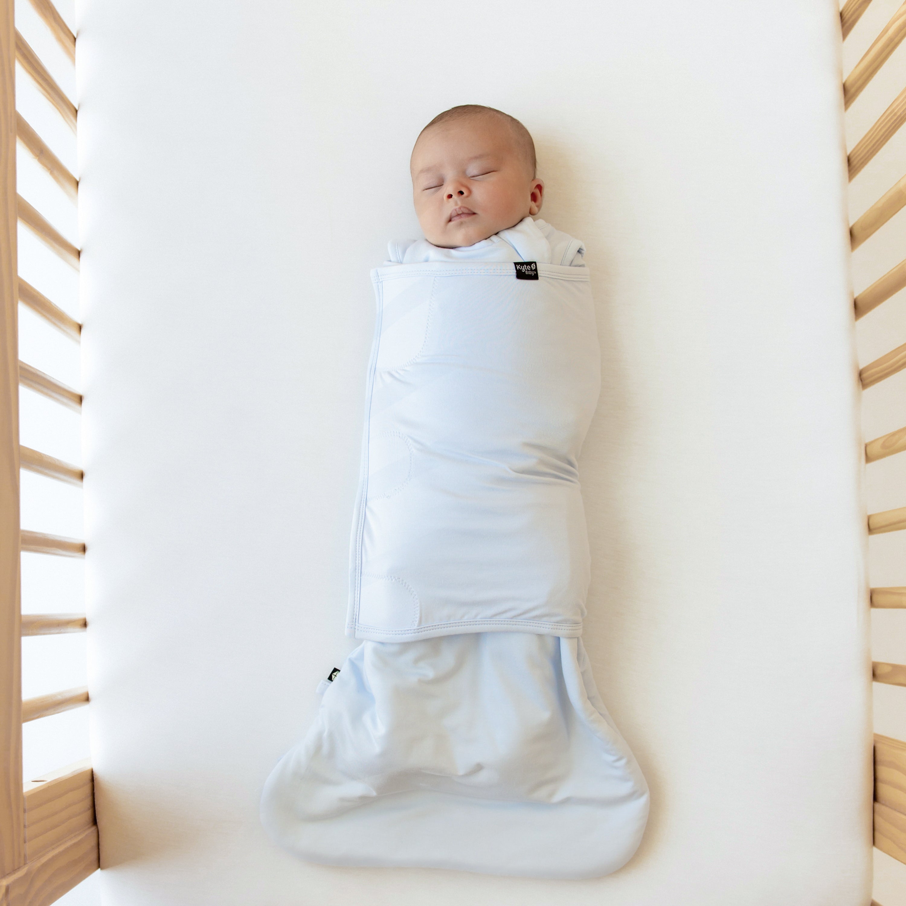 Baby sleeping with both arms in Kyte Baby Sleep Bag Swaddler in Mist 1.0