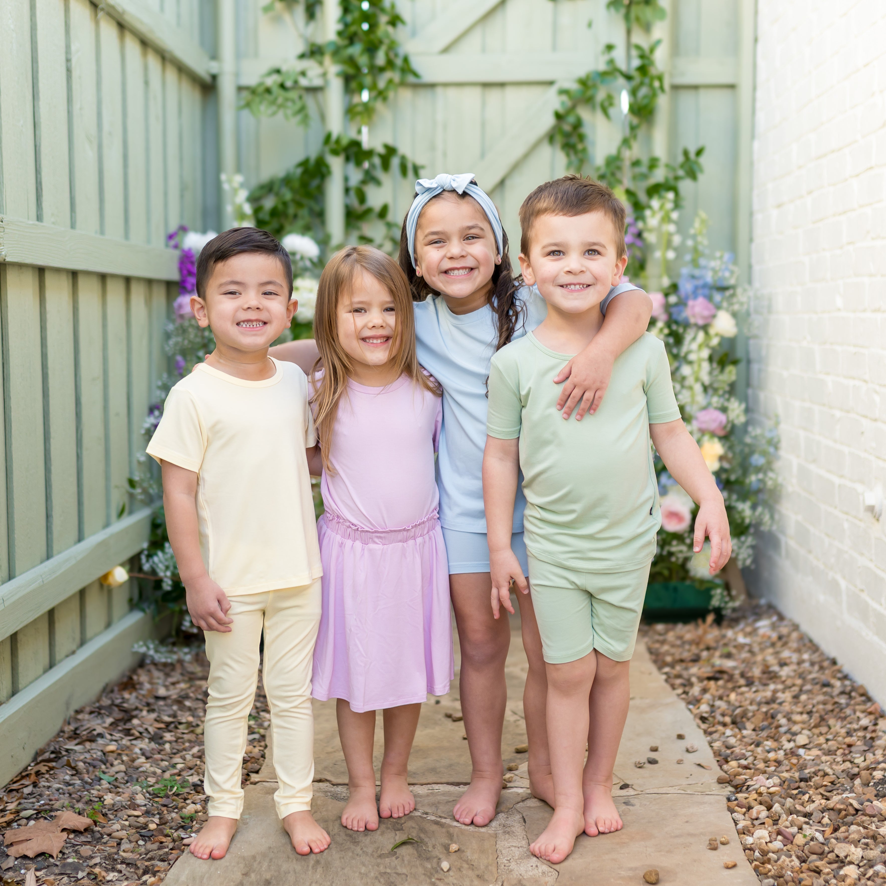 Four smiling children on a stone path outside wearing various items in spring colors