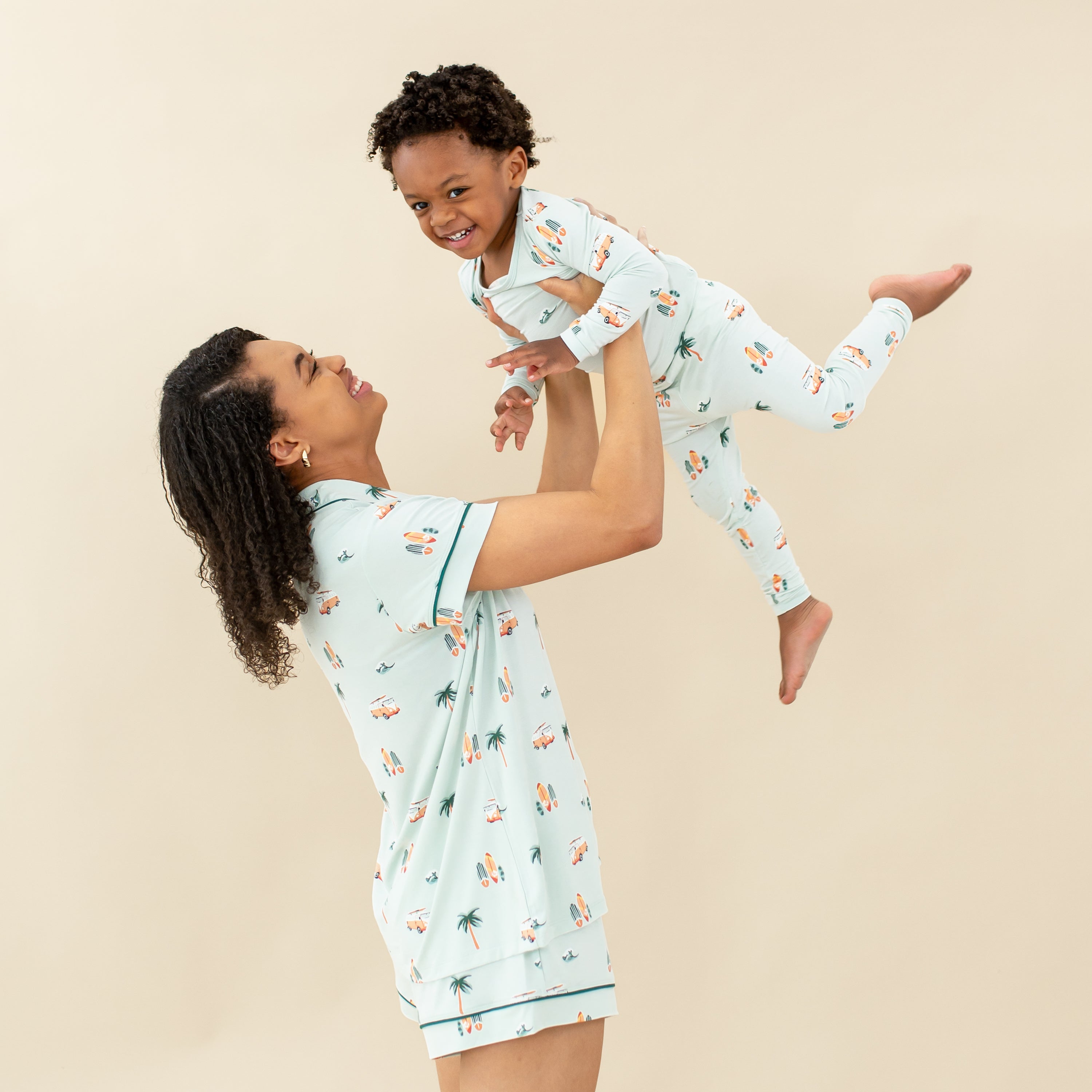 Woman modeling Women's Short Sleeve Pajama Set in Dew Surf holding up toddler wearing matching pajamas