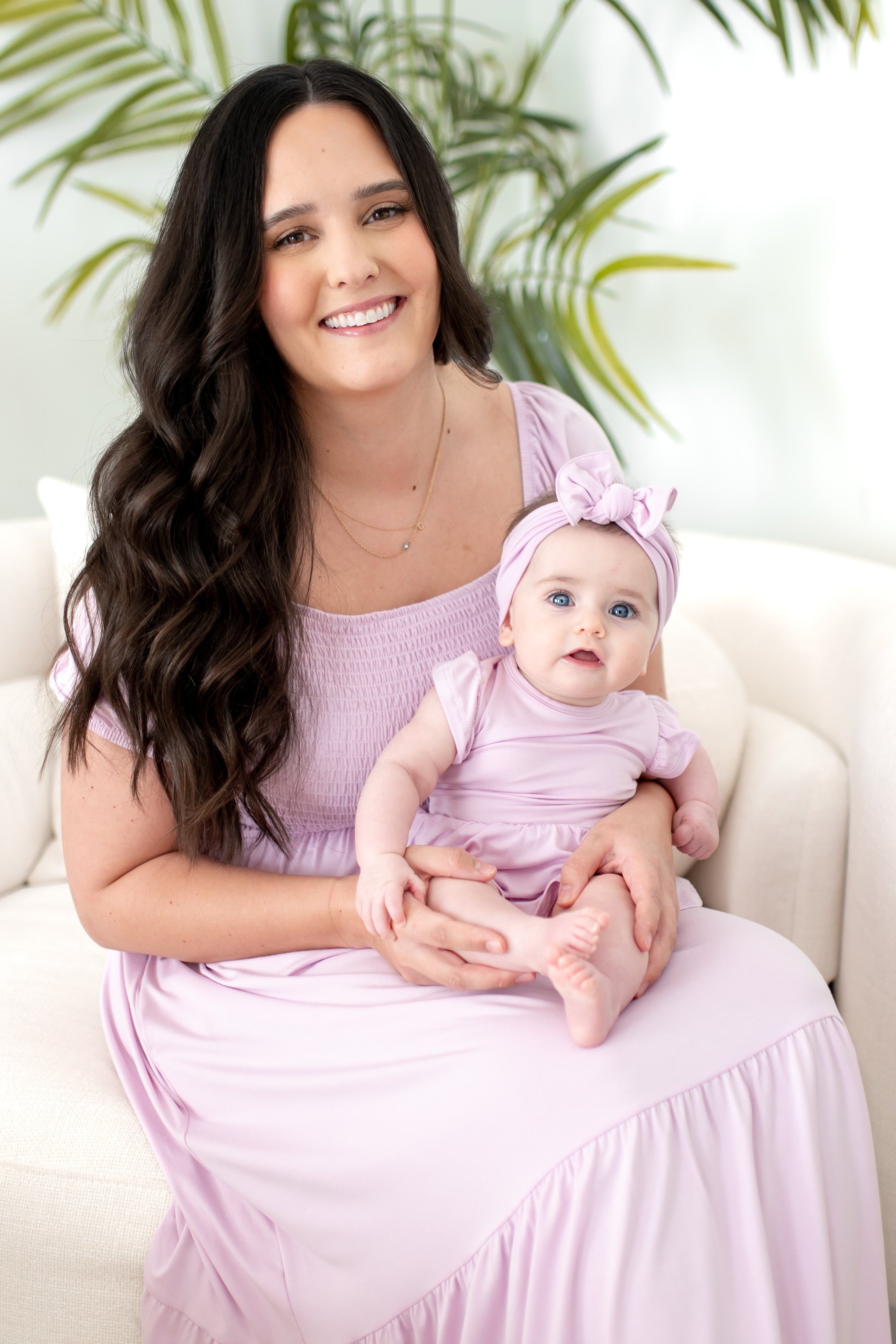 Woman holding a baby wearing matching light purple dresses
