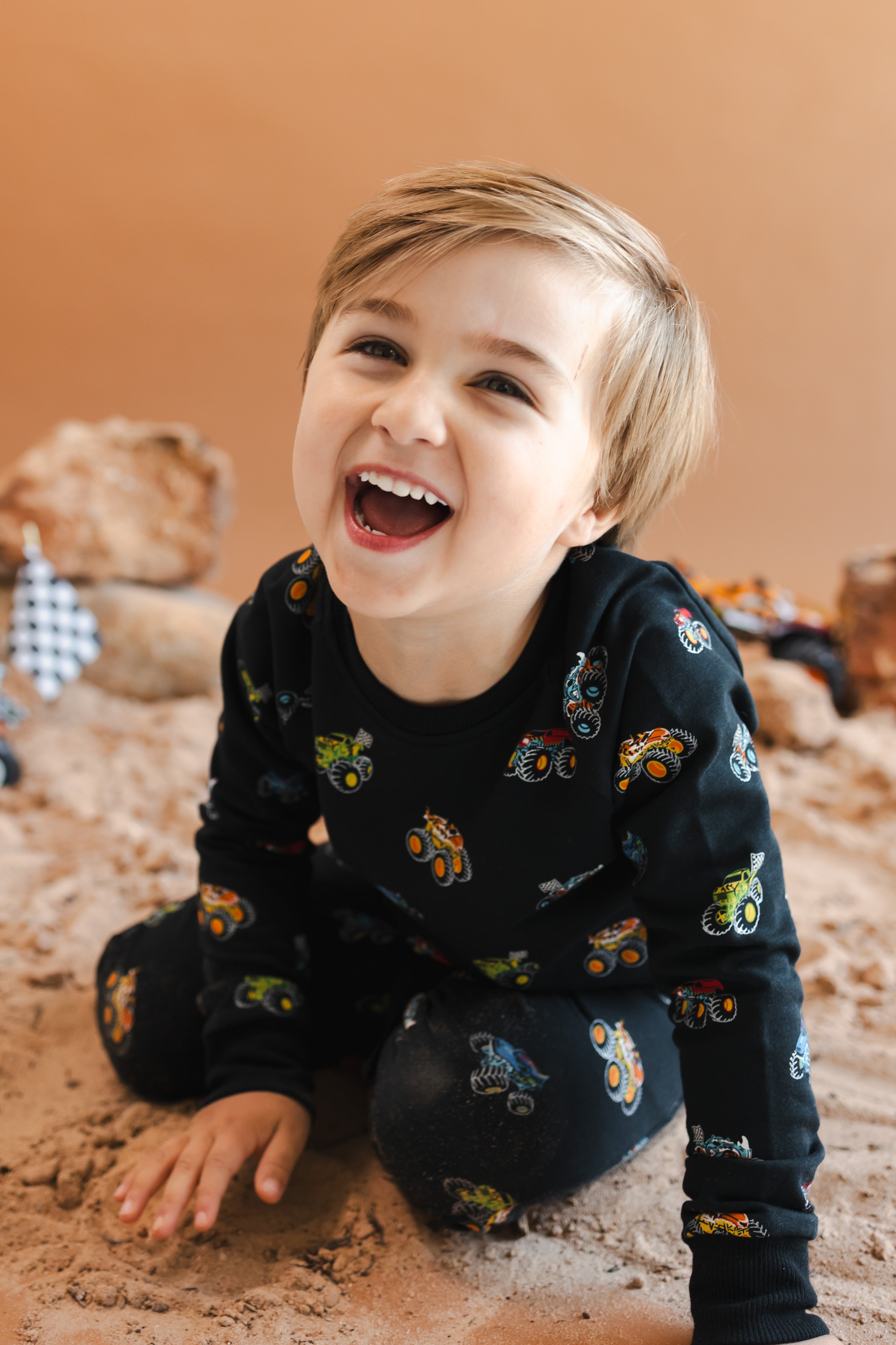 Boy laughing on sand wearing black Long Sleeve Jogger Set in Monster Truck print