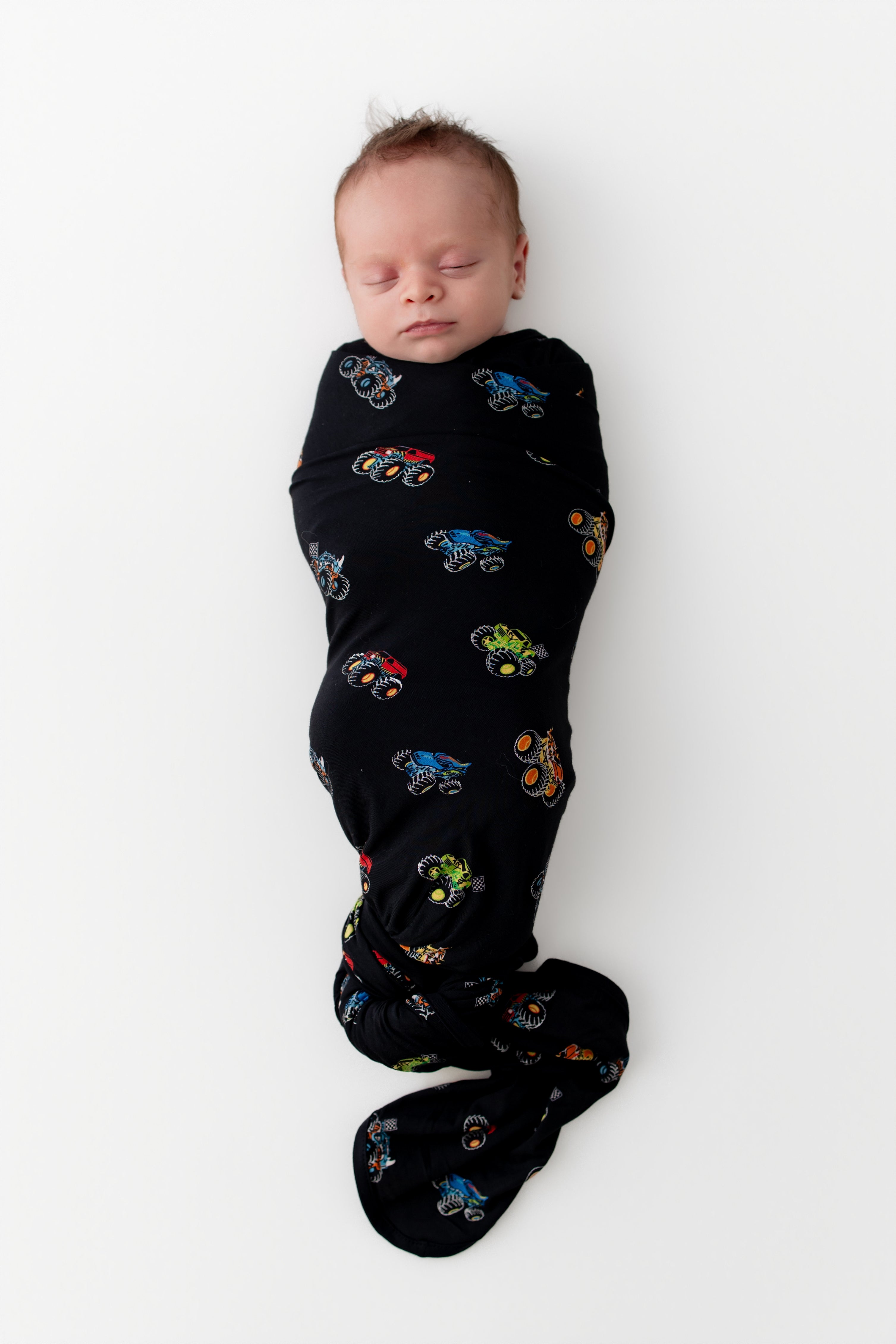 Baby sleeping in Black Swaddle Blanket in Monster Truck print on white background