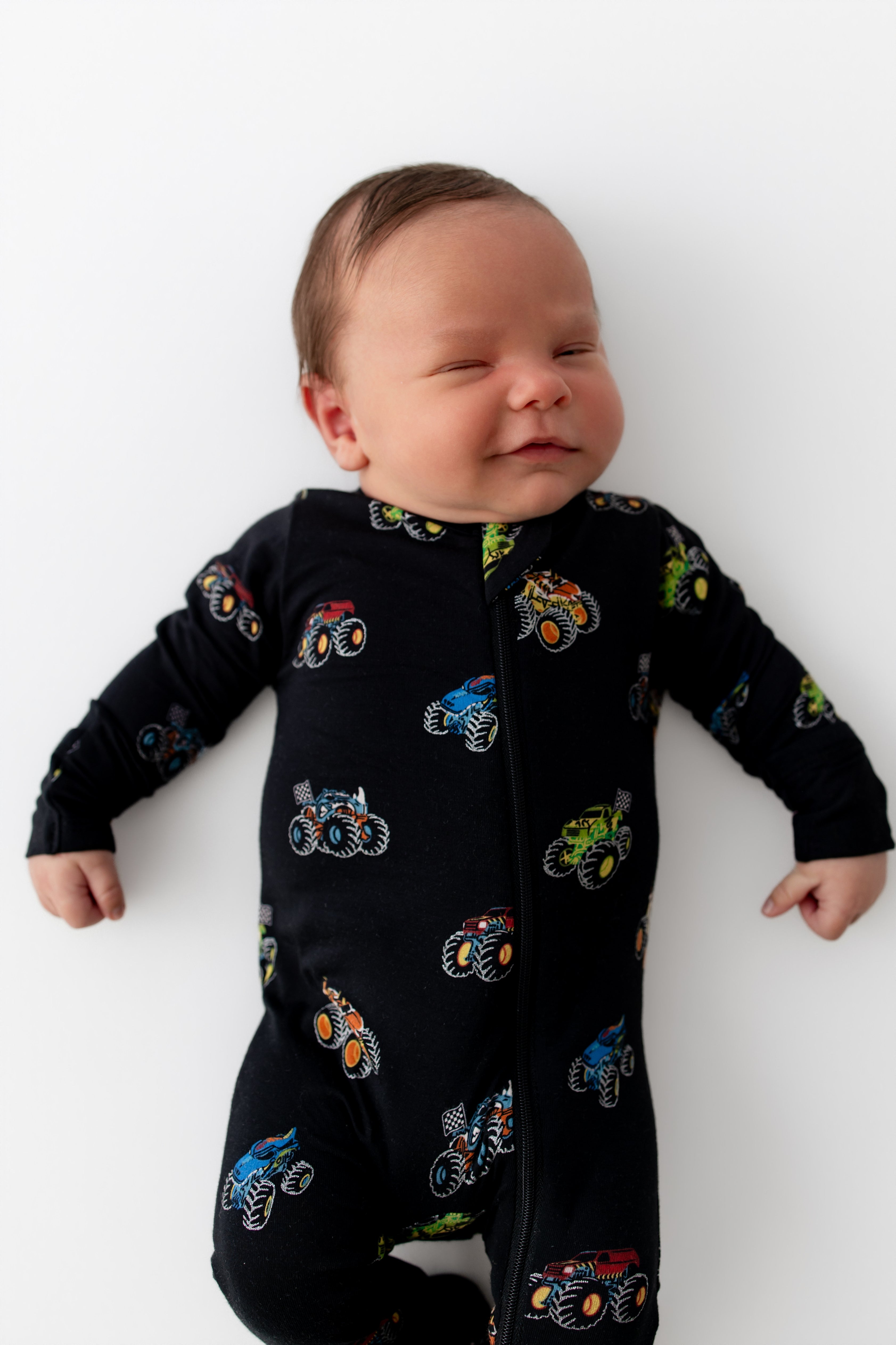 Baby wearing Black Zippered Footie in Monster Truck print on white background